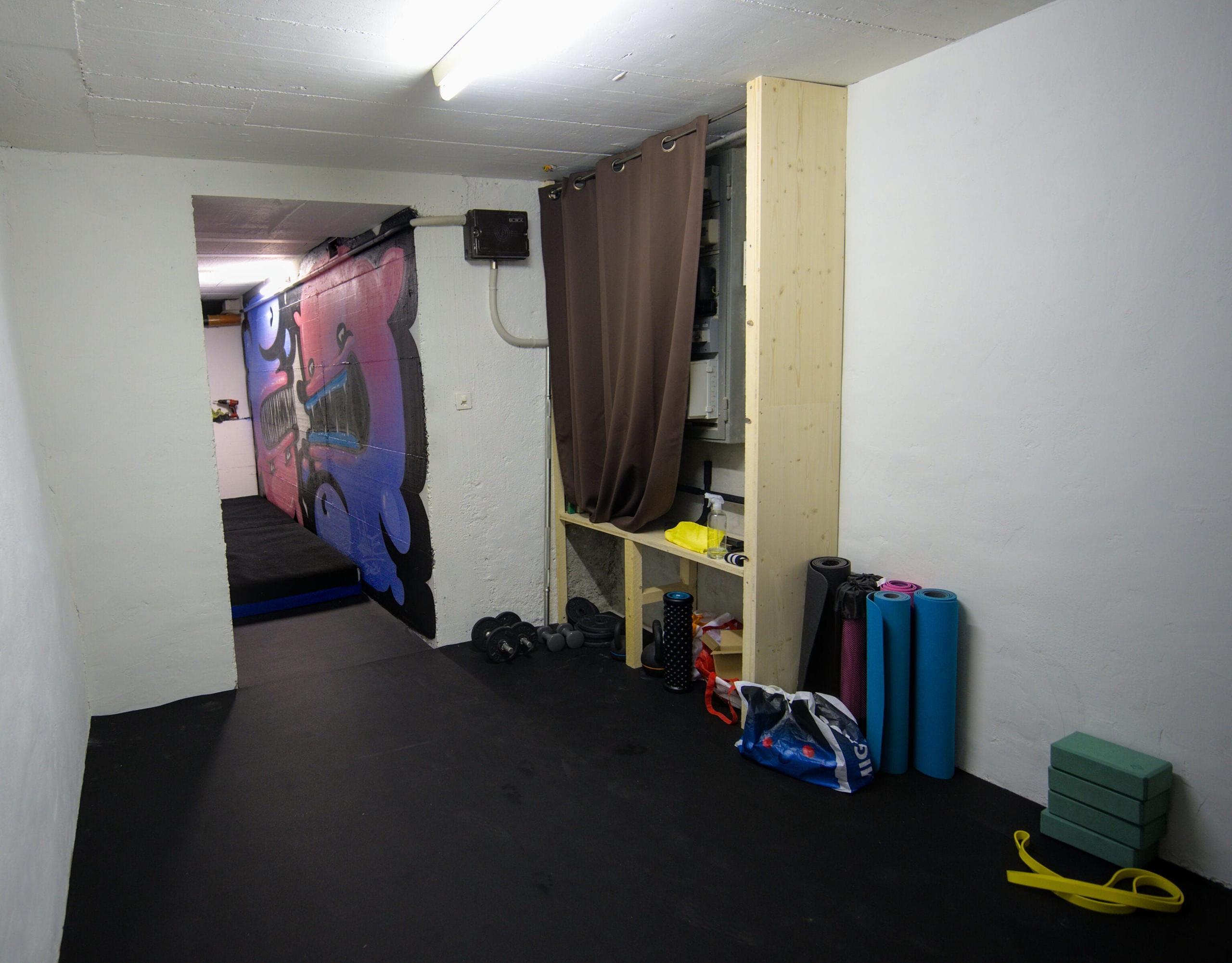 The gym room in the basement of Alpiness coliving, with yoga mats, weights, and fitness equipment.