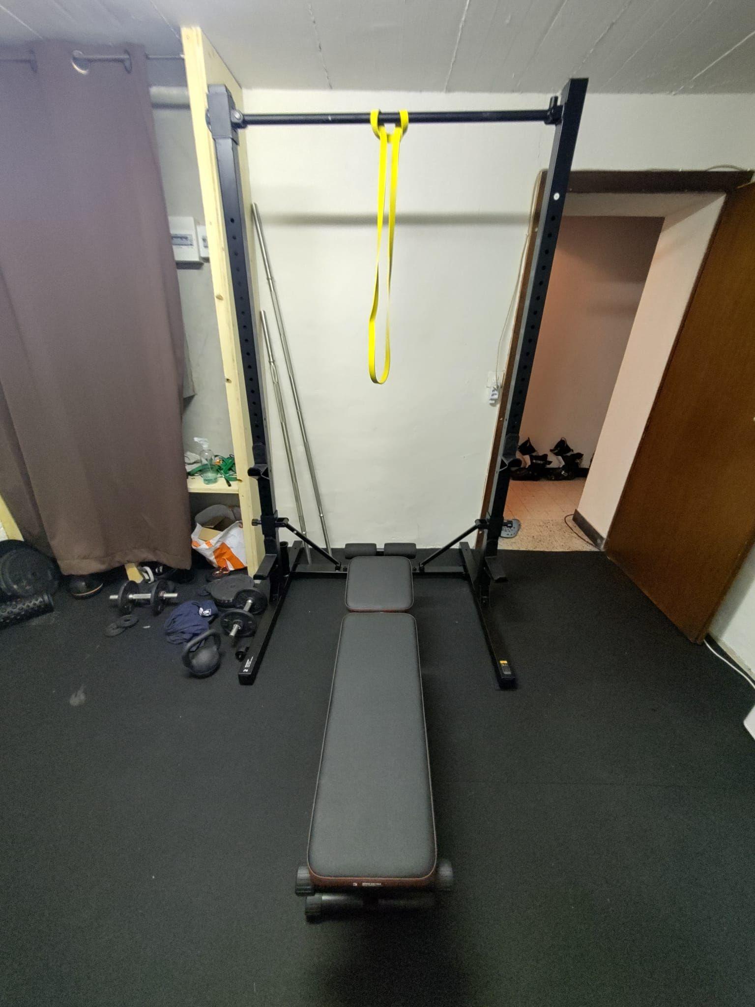 The squat rack and weight bench in the Alpiness gym room, with various weight plates.