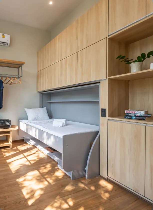 Compact Flexie room with a fold-up single bed integrated into wooden cabinetry with shelving and storage