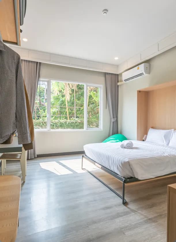 Spacious room with a queen-size bed, large windows overlooking greenery, air conditioning, and wooden furniture