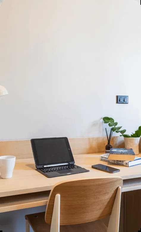 Minimalist wooden desk with a laptop, books, and a small plant, with a wooden headboard panel behind
