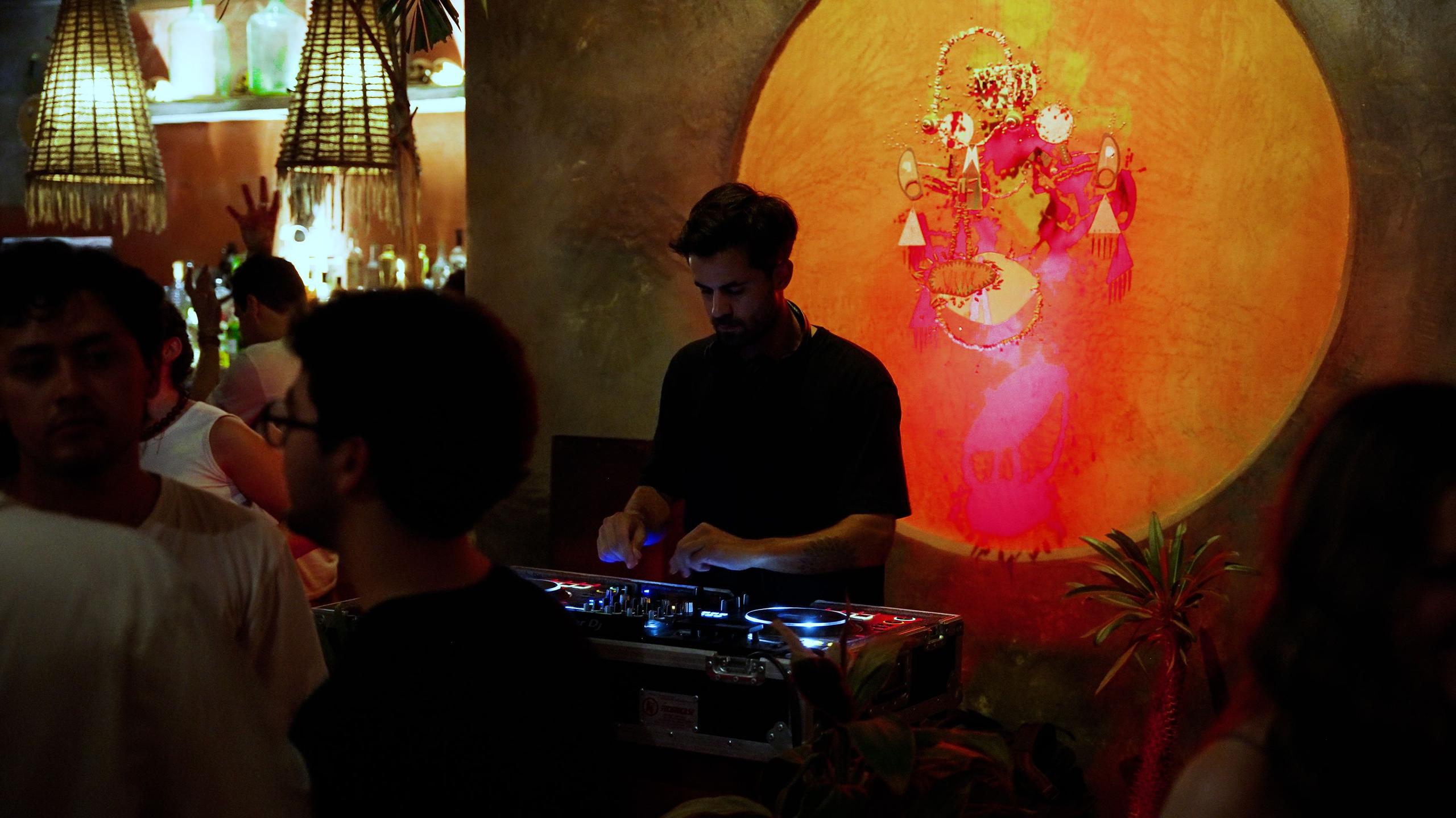 DJ performing at a bar or nightclub in Puerto Escondido, with guests dancing in the background