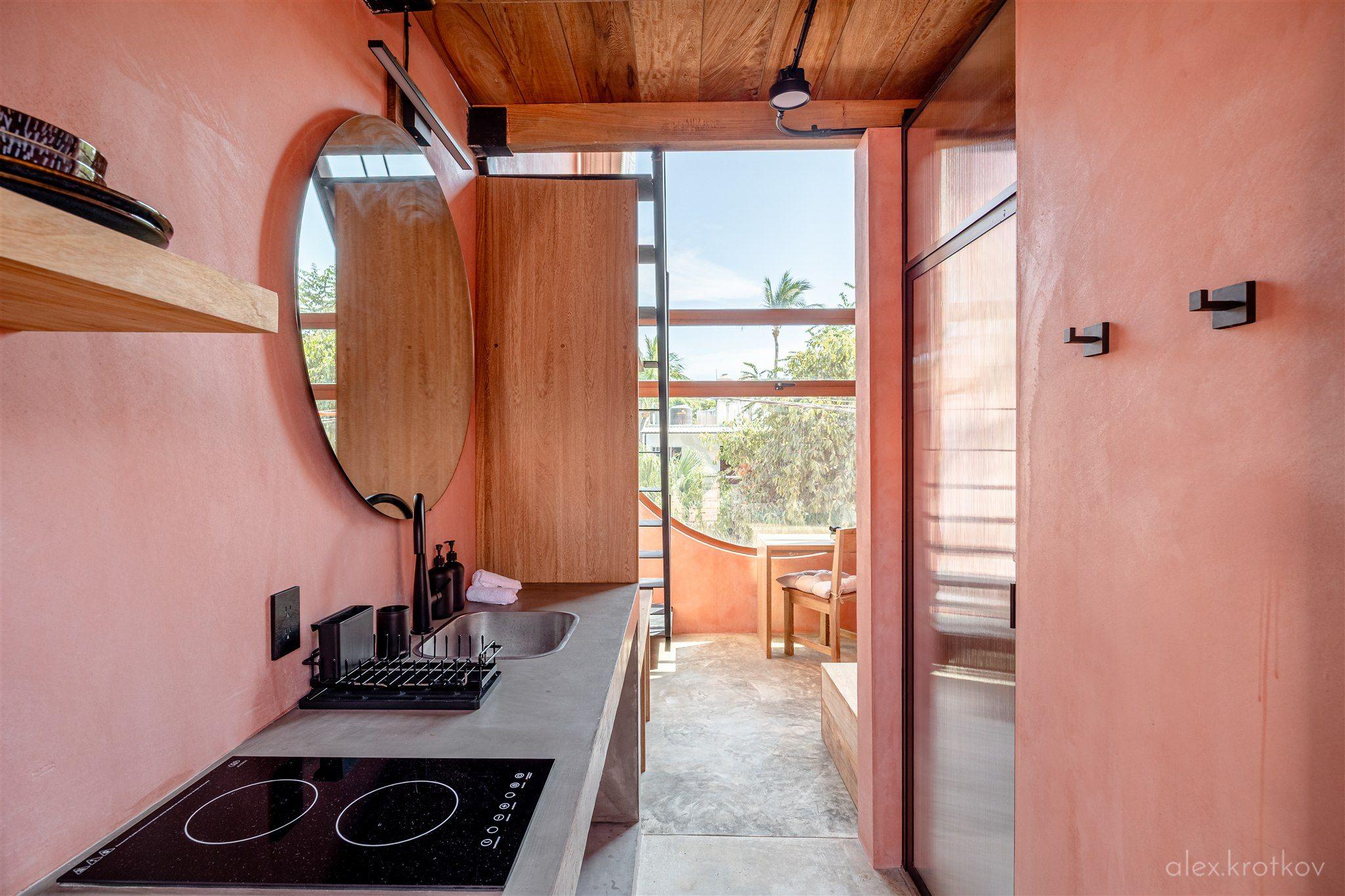 Private kitchenette area of the Classic King Loft at Amplitude Coliving, with an induction cooktop, sink, round mirror, and view to the terrace
