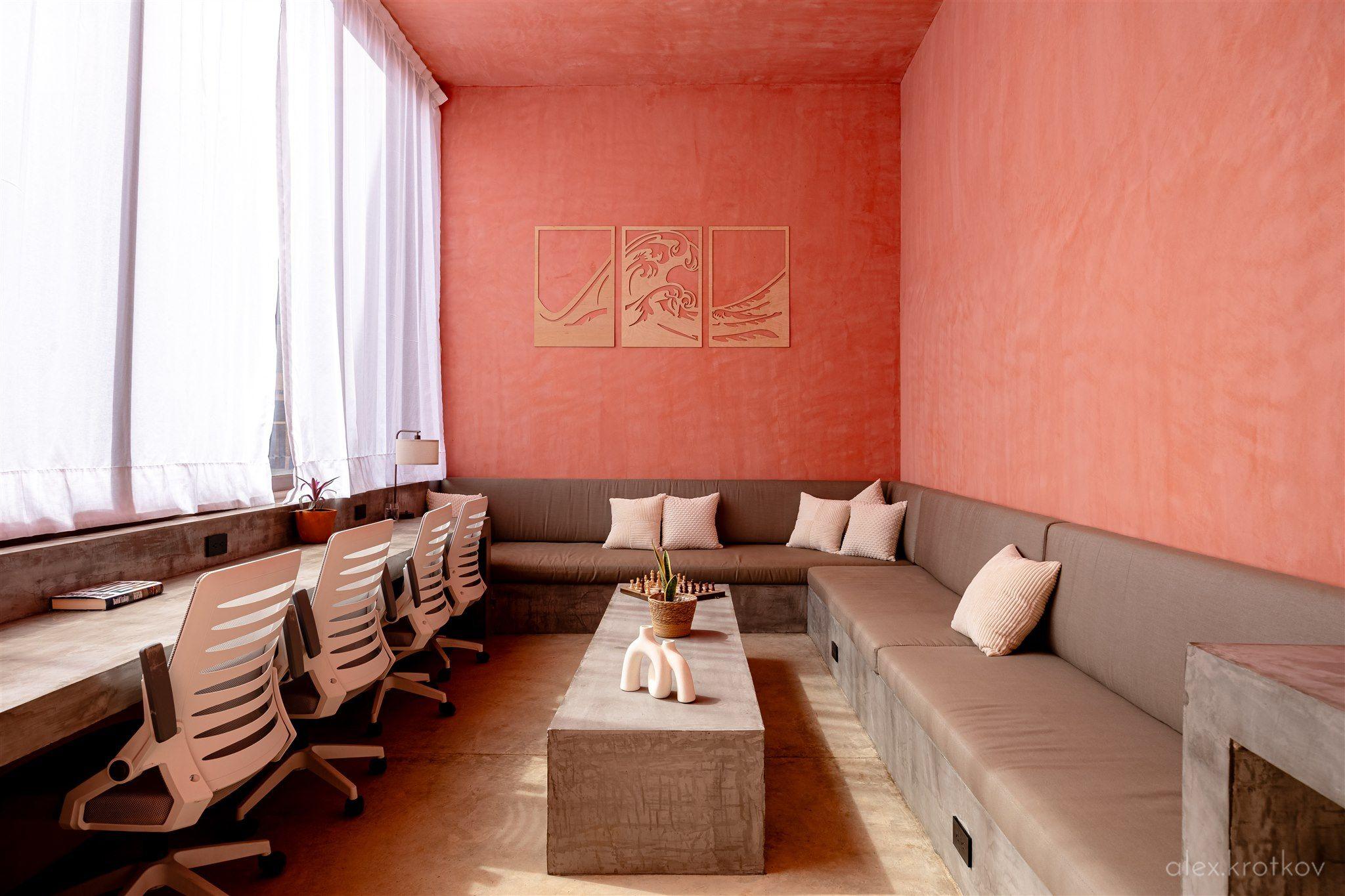 Wide view of the air-conditioned coworking lounge at Amplitude Coliving, showing the long desk with ergonomic chairs, large corner sofa, and wave-motif wall art