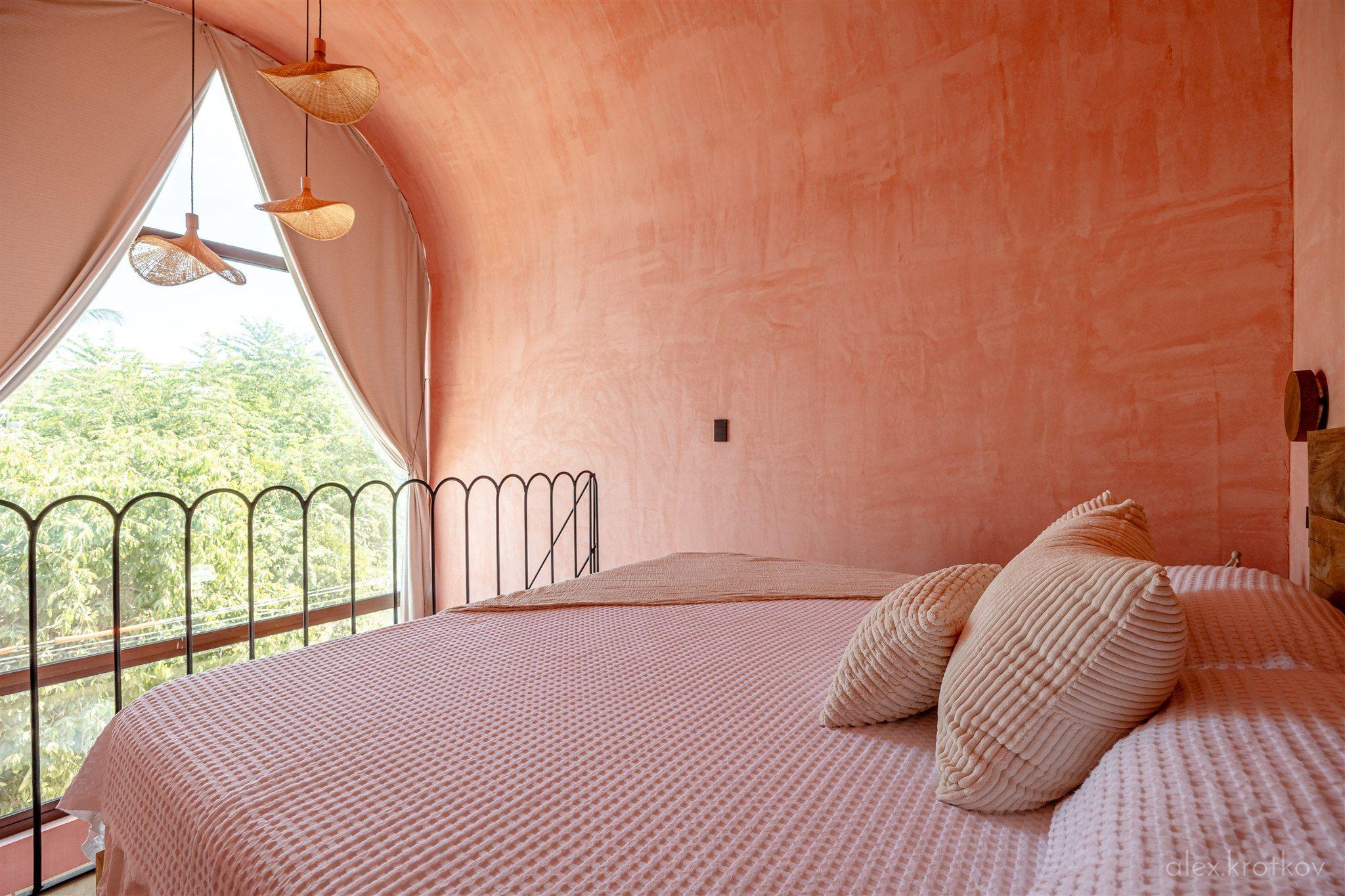 Bedroom of the Arched King Loft room at Amplitude Coliving, featuring a king bed under a distinctive arched ceiling with a large arched window overlooking greenery