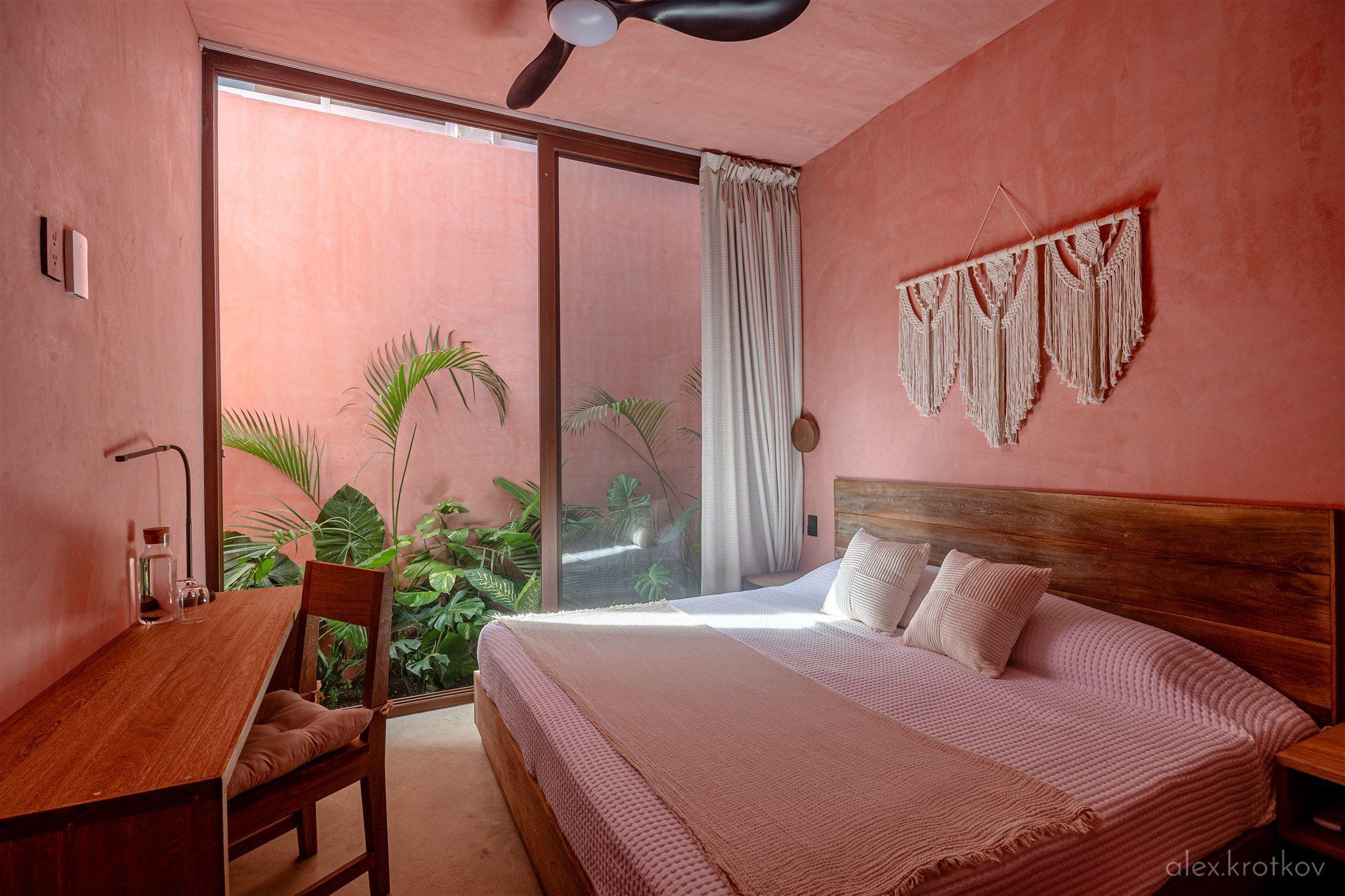 Garden King Room at Amplitude Coliving, featuring a king bed, wooden desk, macramé wall hanging, and large sliding glass door with garden view