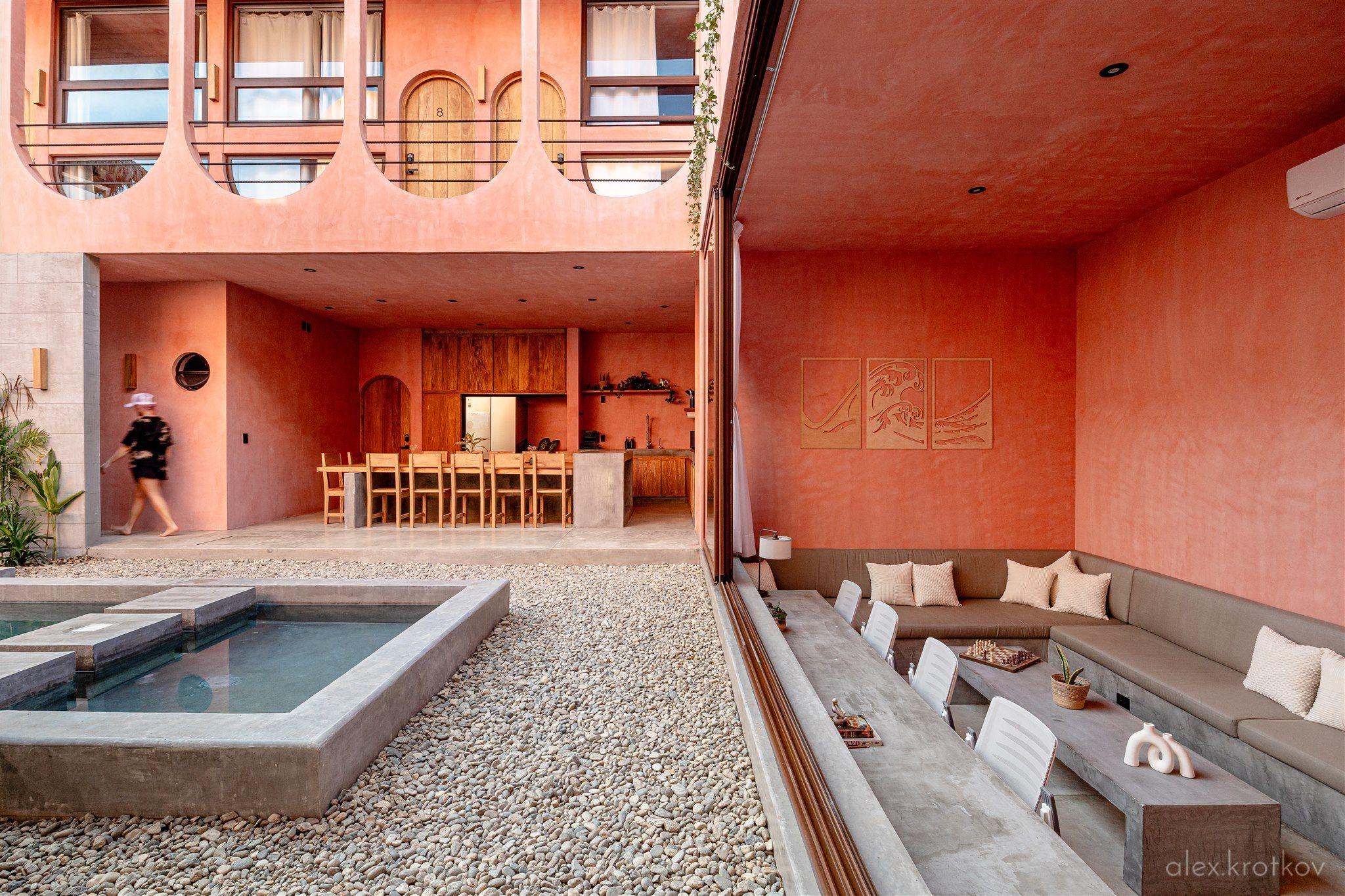 Wide view of the Amplitude Coliving courtyard showing the pool, outdoor lounge seating, and open-plan shared kitchen in the background