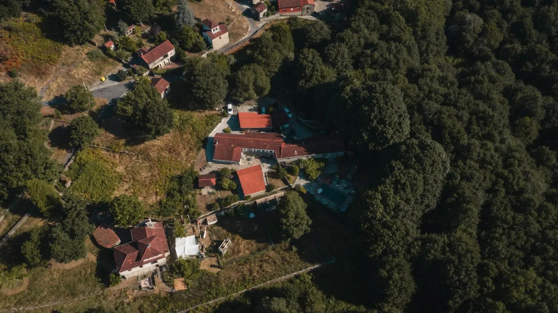 Aerial drone view of the Anceu Coliving property surrounded by Galician forest, showing the buildings with red-tiled roofs
