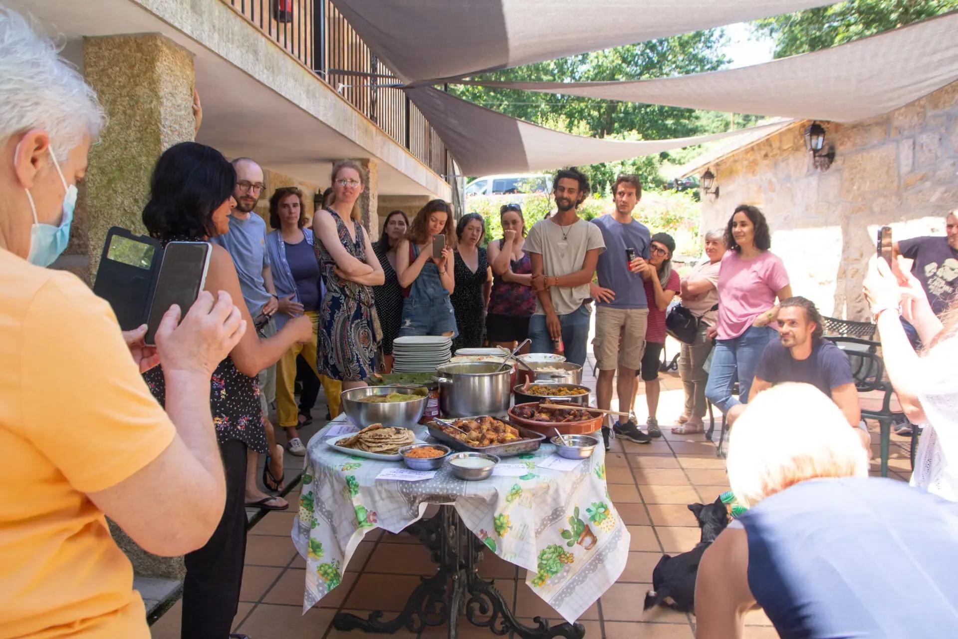 Group of colivers gathered around a table with food on the covered terrace, with someone photographing the spread
