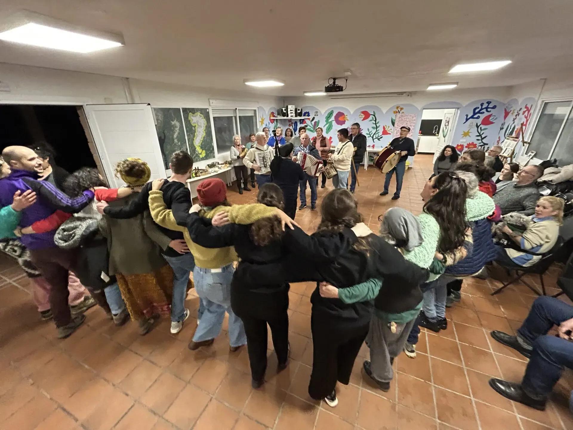 Large group of people dancing in a circle in a decorated indoor space with murals on the walls