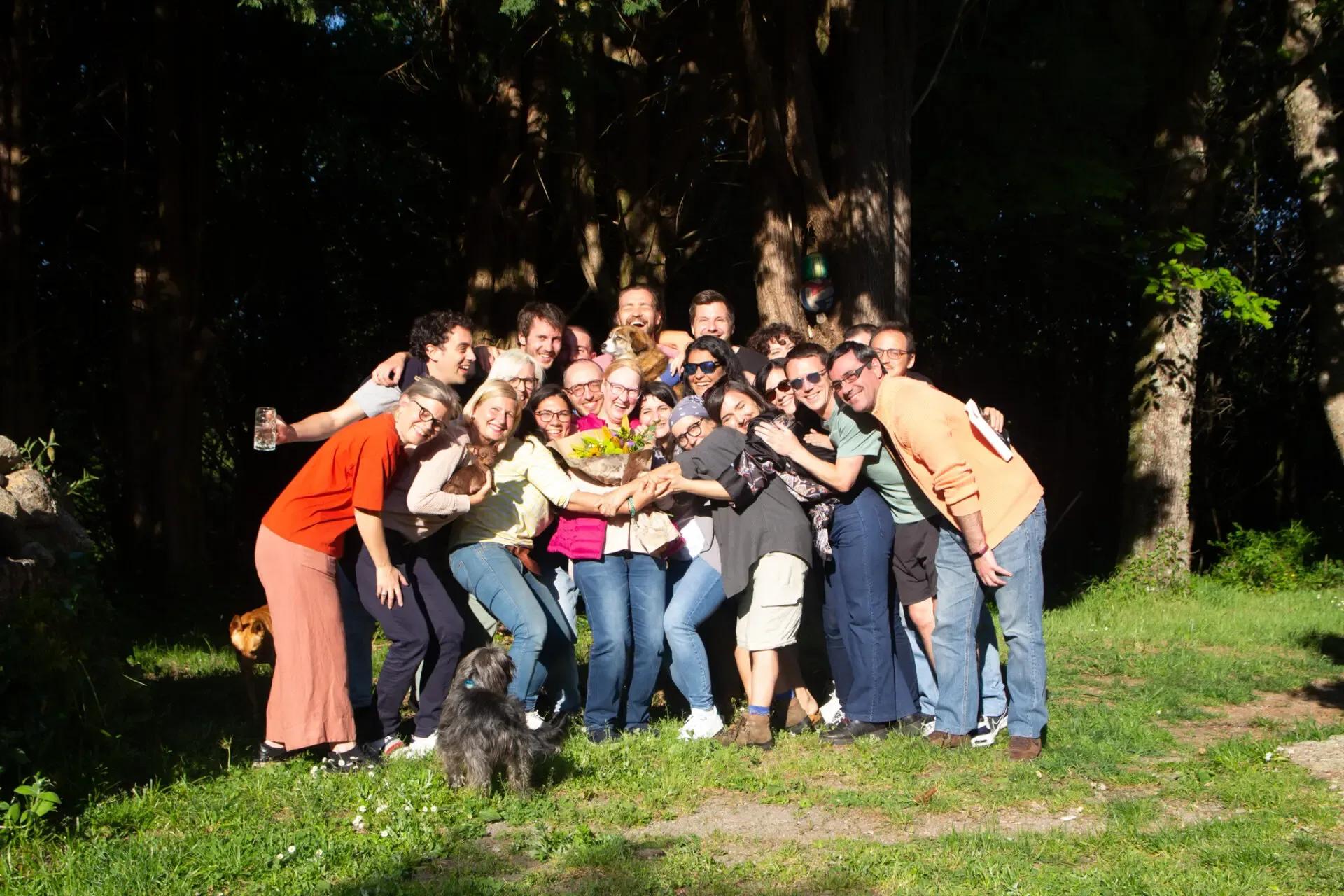 Large group of colivers celebrating together outdoors in the forest, gathered around a bouquet of flowers