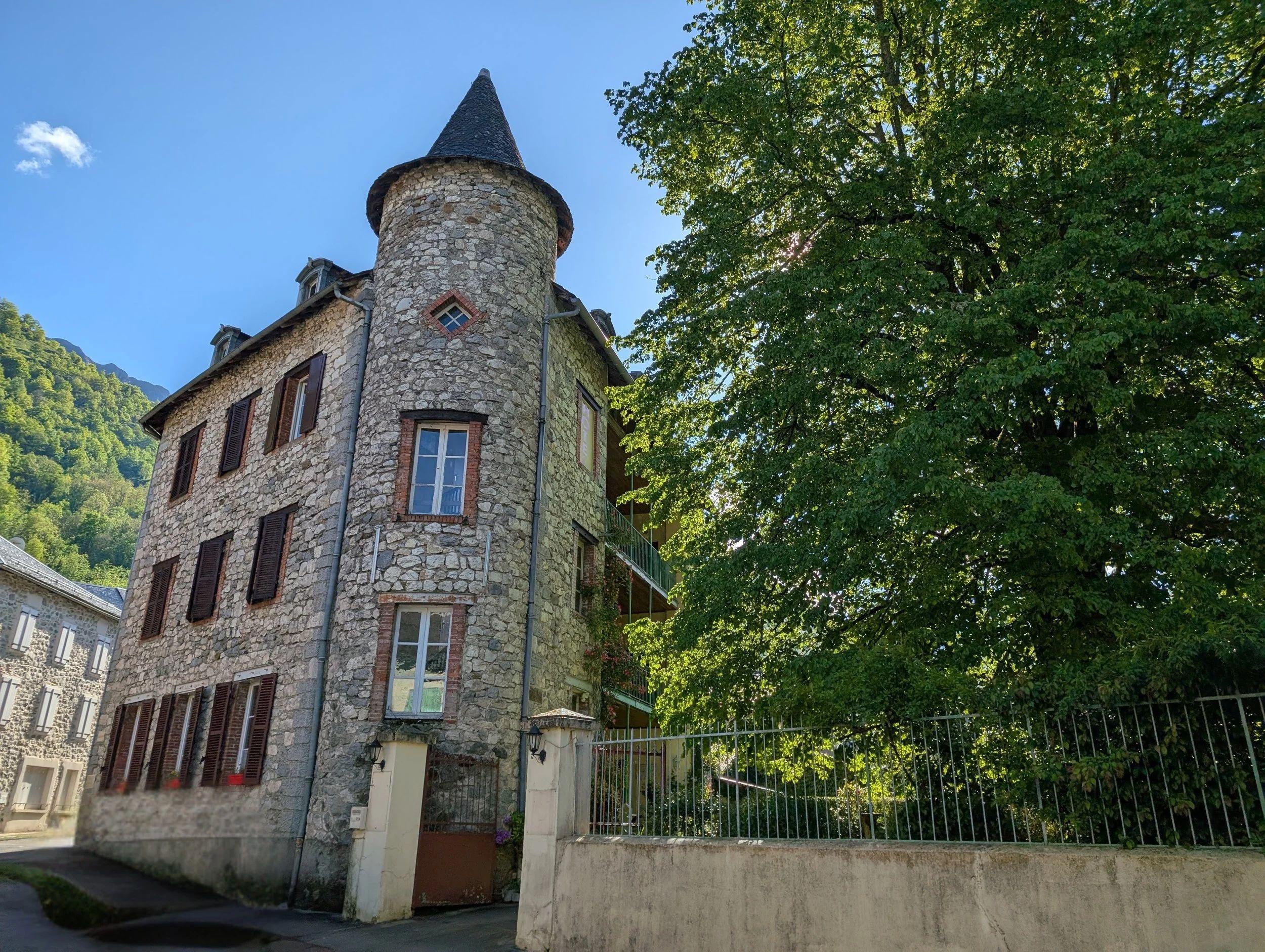 Exterior view of the Aulus Coliving building — a stone building with a turret, surrounded by trees and mountains