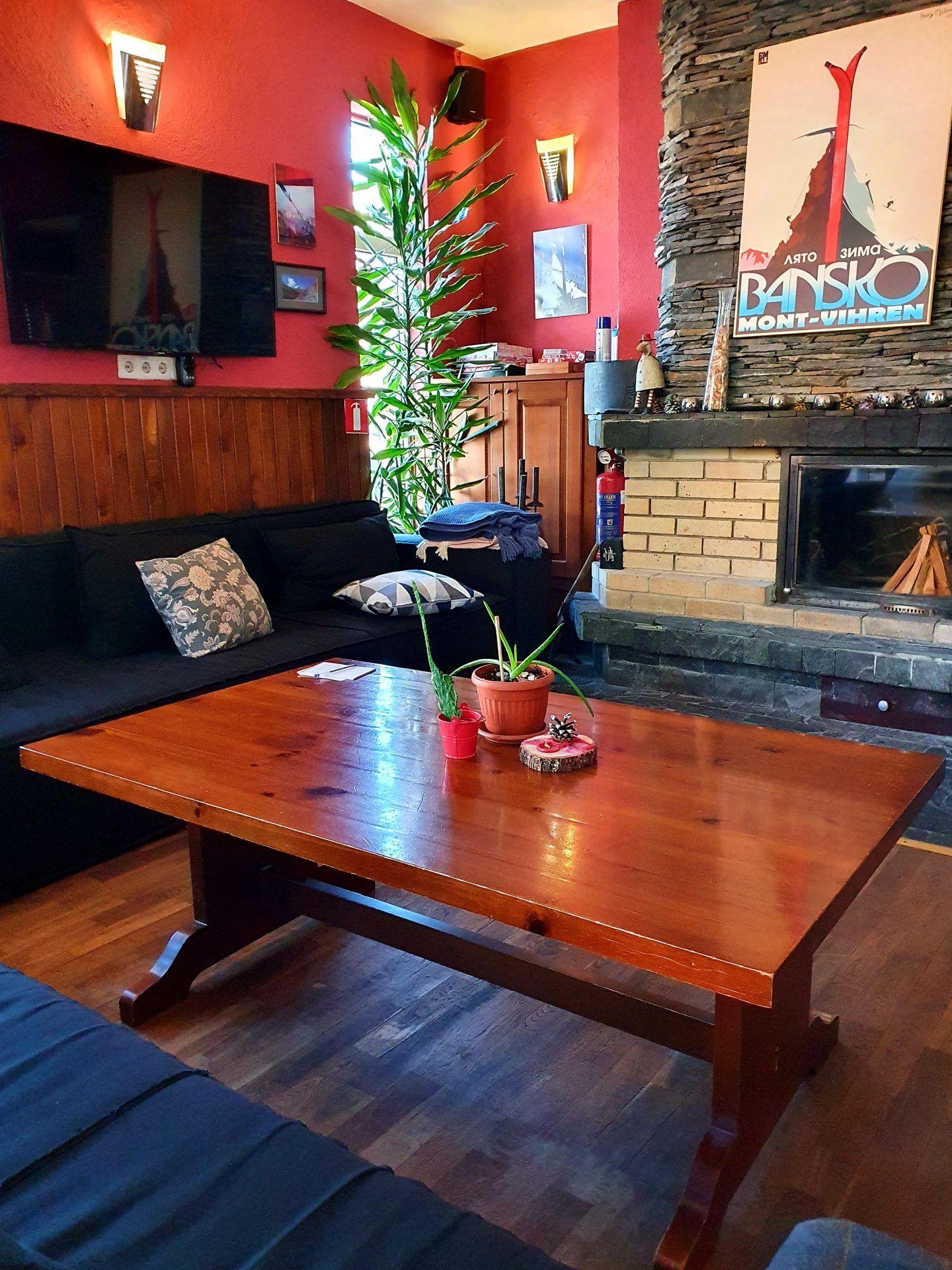 The Avalon living room coworking area with sofas, a wooden coffee table, plants, and a stone fireplace with a Bansko ski poster