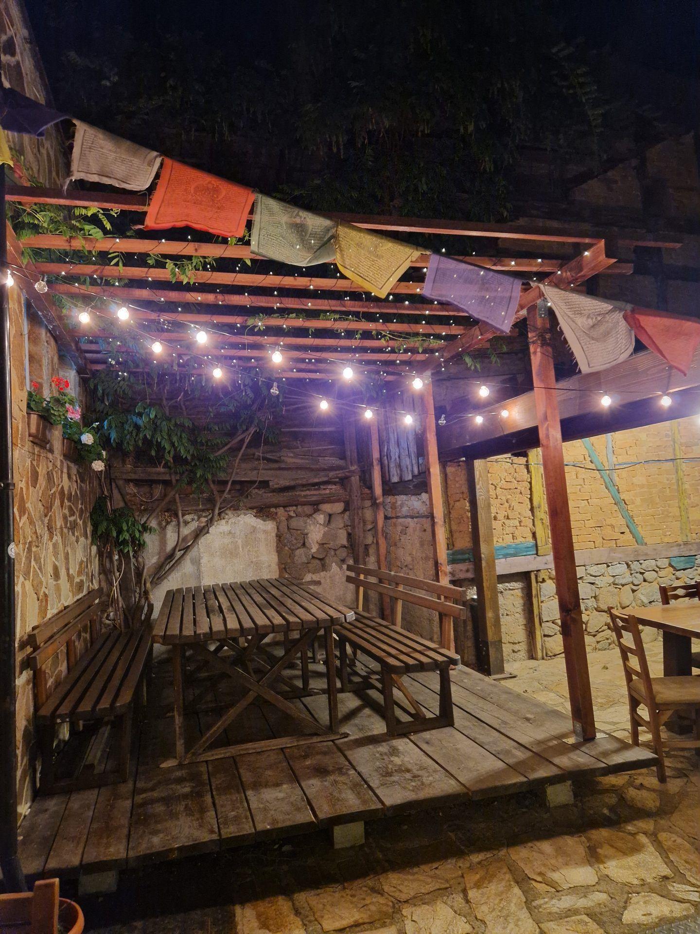 The Avalon garden at night with wooden pergola, fairy lights, and prayer flags