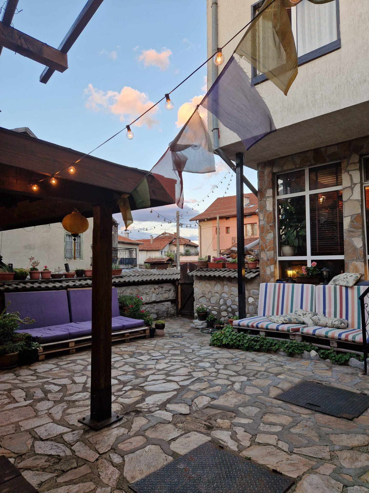 The Avalon garden with stone paving, outdoor sofas, fairy lights, and prayer flags at dusk