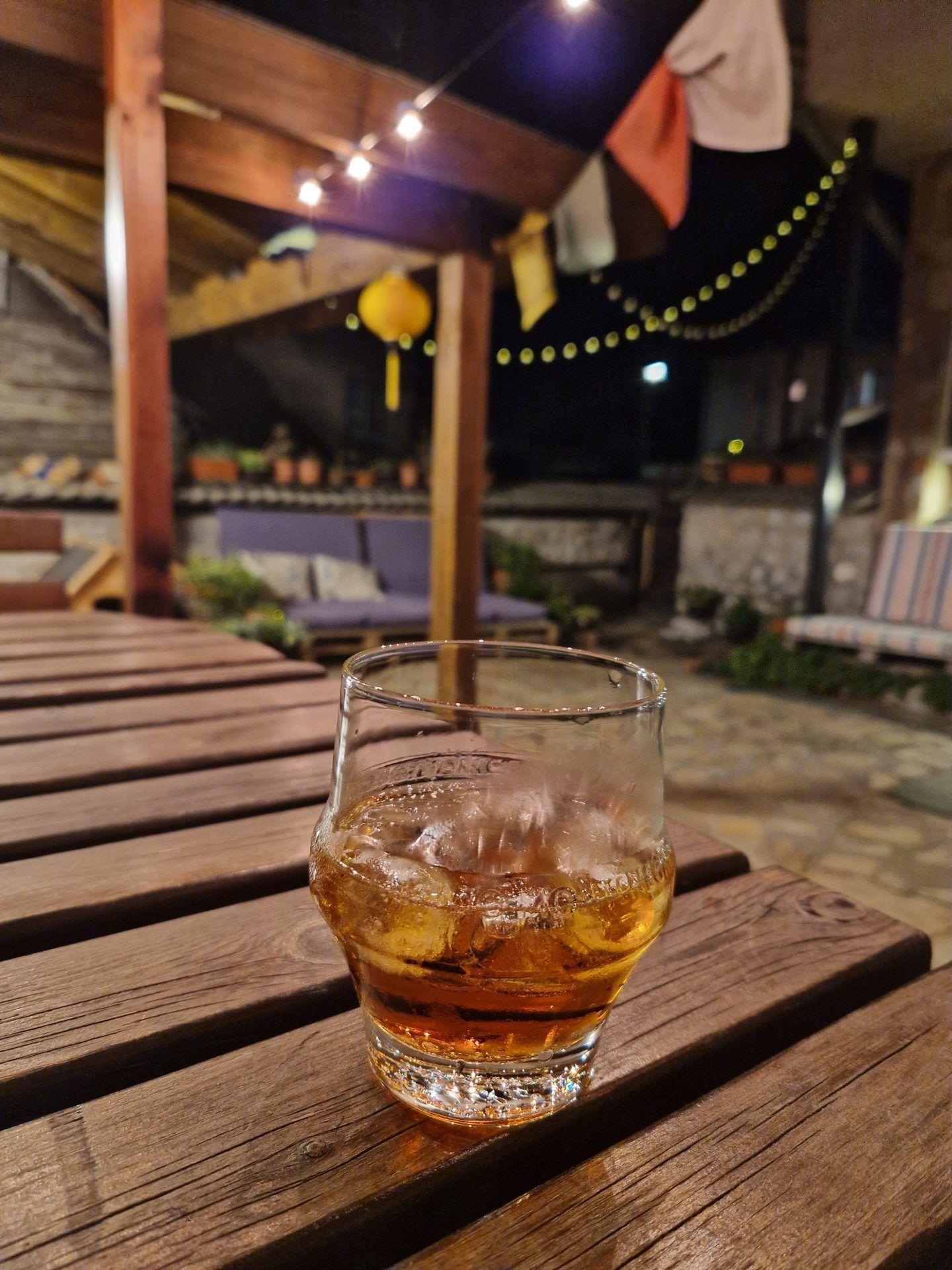 A glass of whisky on a wooden table in the Avalon garden at night with fairy lights