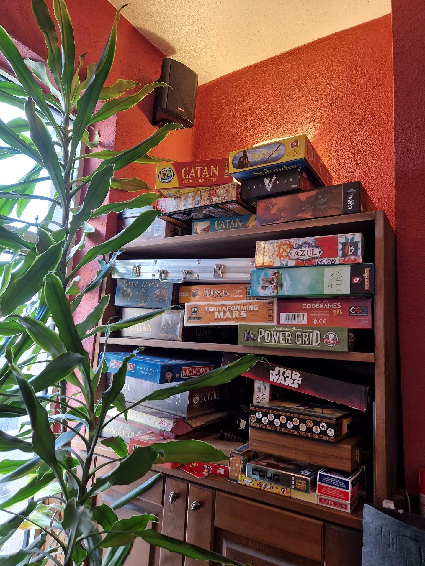 A shelf stocked with board games including Catan, Terraforming Mars, Azul, and many others in the communal area
