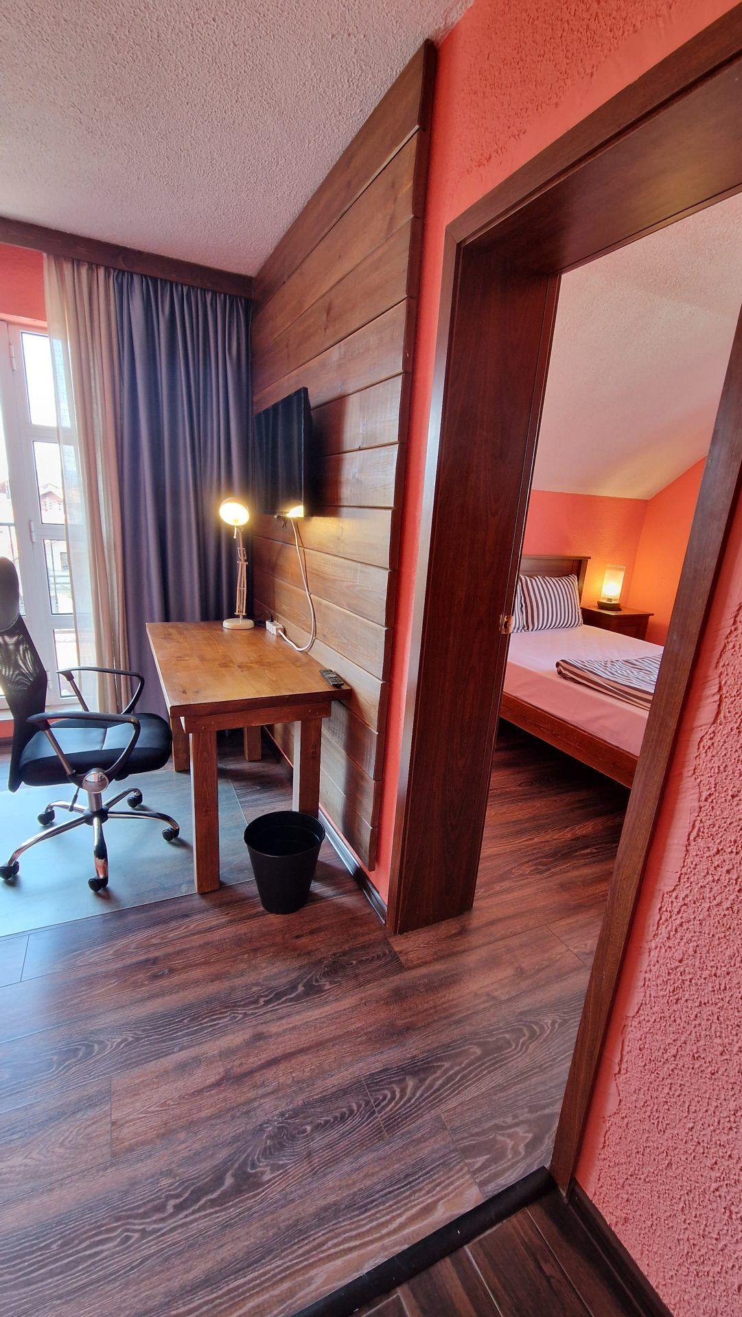 The separate office/living area of a mini apartment with a desk, office chair, and view into the bedroom