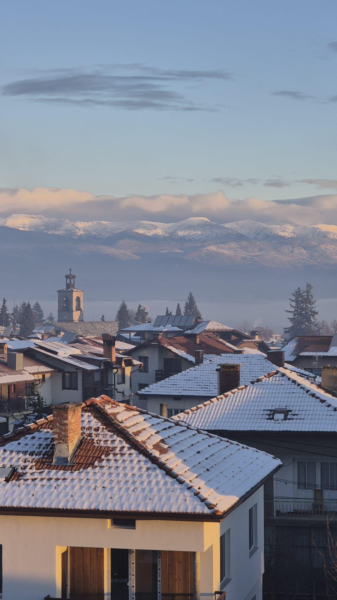 Winter view over snow-covered Bansko rooftops with mountains in the background at sunrise