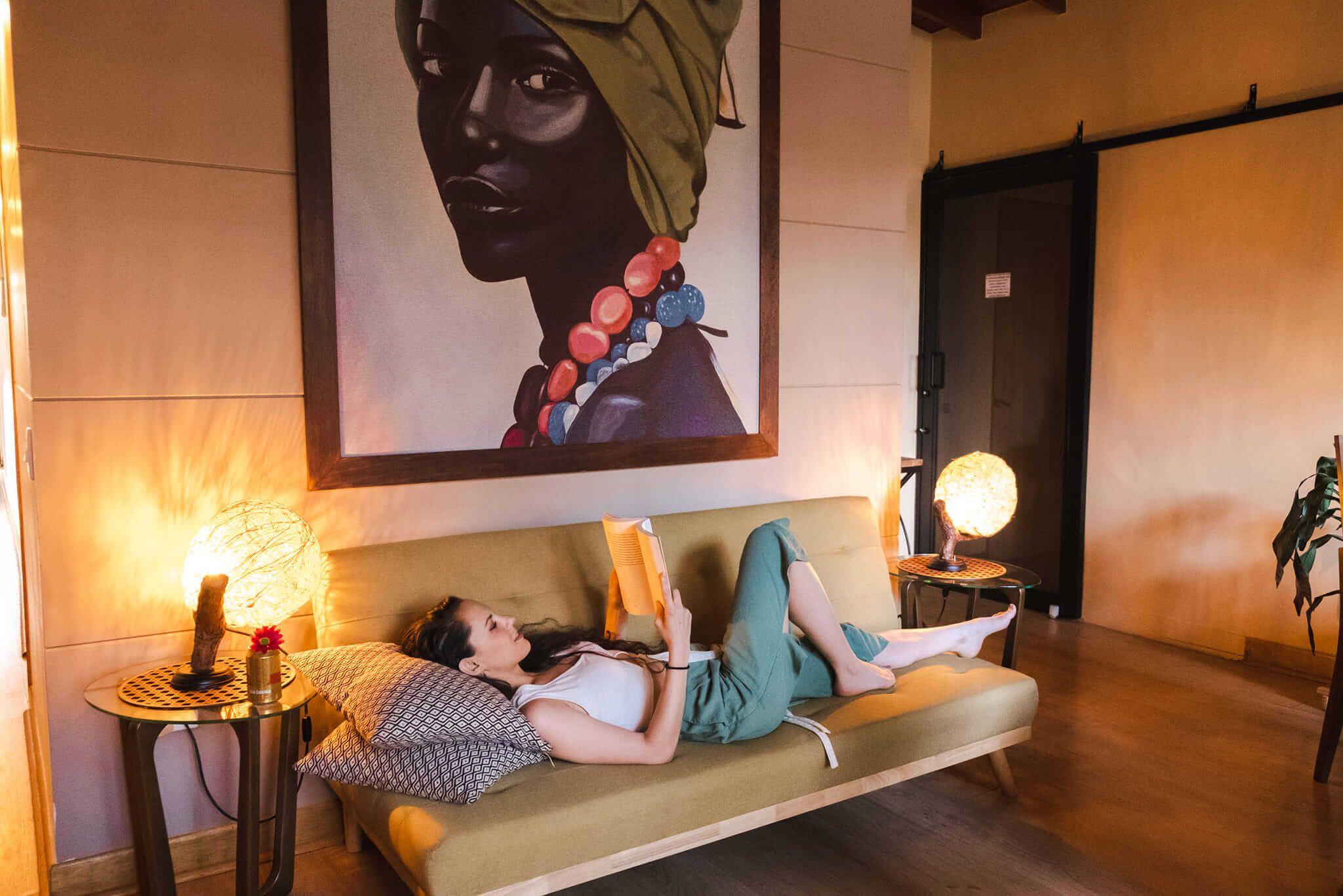 A guest lying on a sofa reading a book in the cosy living room with warm lighting and artwork on the wall