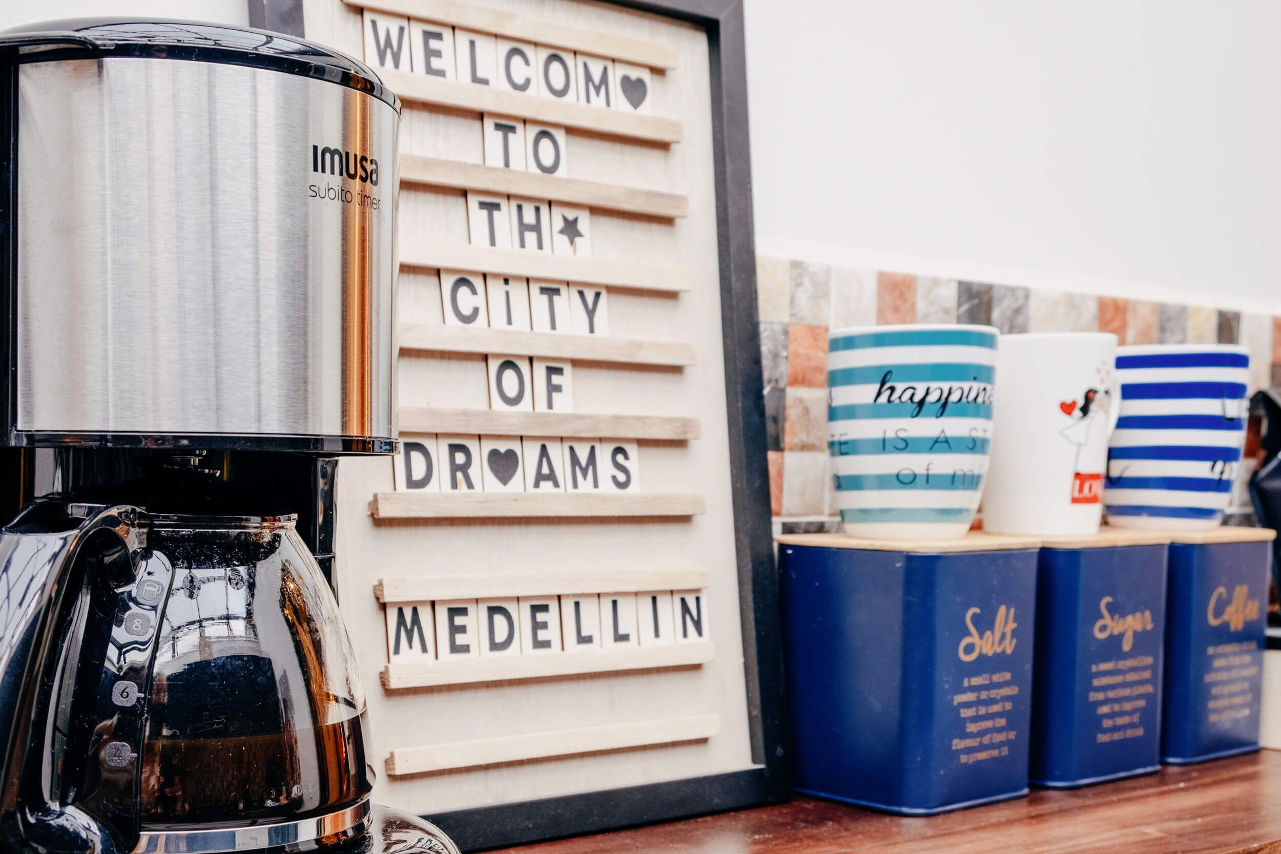 Kitchen counter with a coffee machine, mugs, and a letter board sign reading 'Welcome to the City of Dreams Medellín'