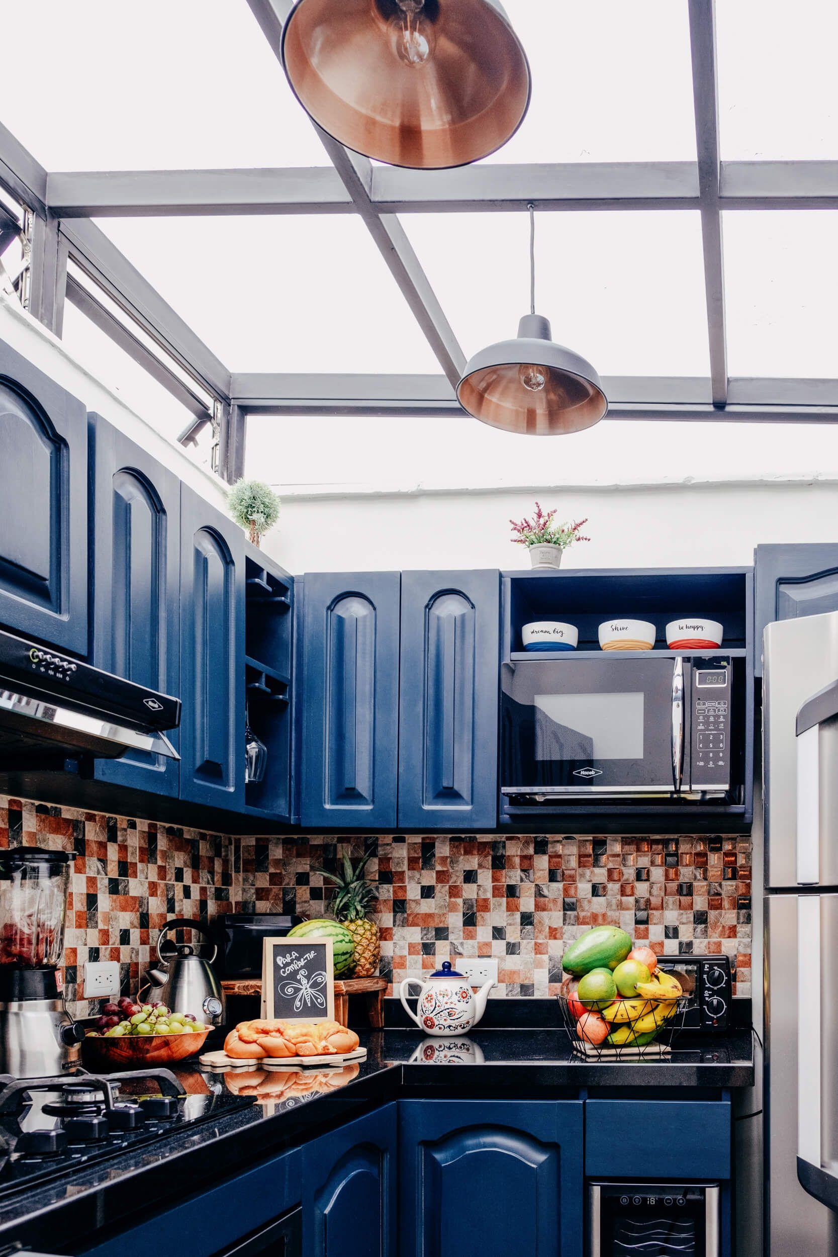 Fully equipped shared kitchen with bold blue cabinets, mosaic tile backsplash, fresh fruit, and a skylight ceiling
