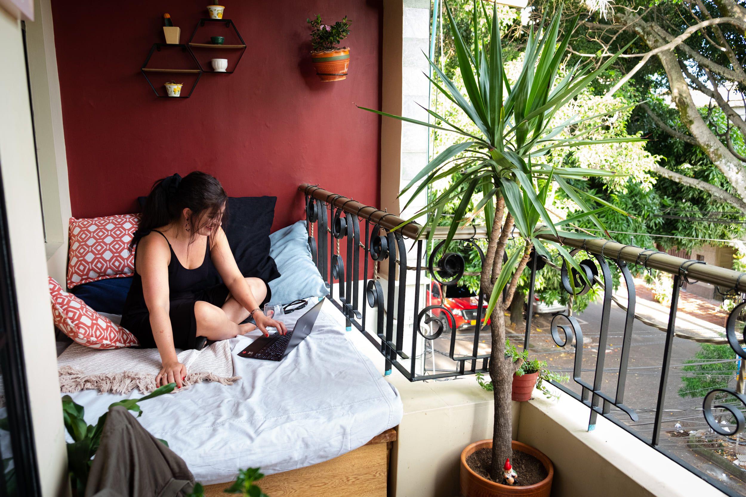 A guest working on a laptop on the shared balcony with lush plants and street view