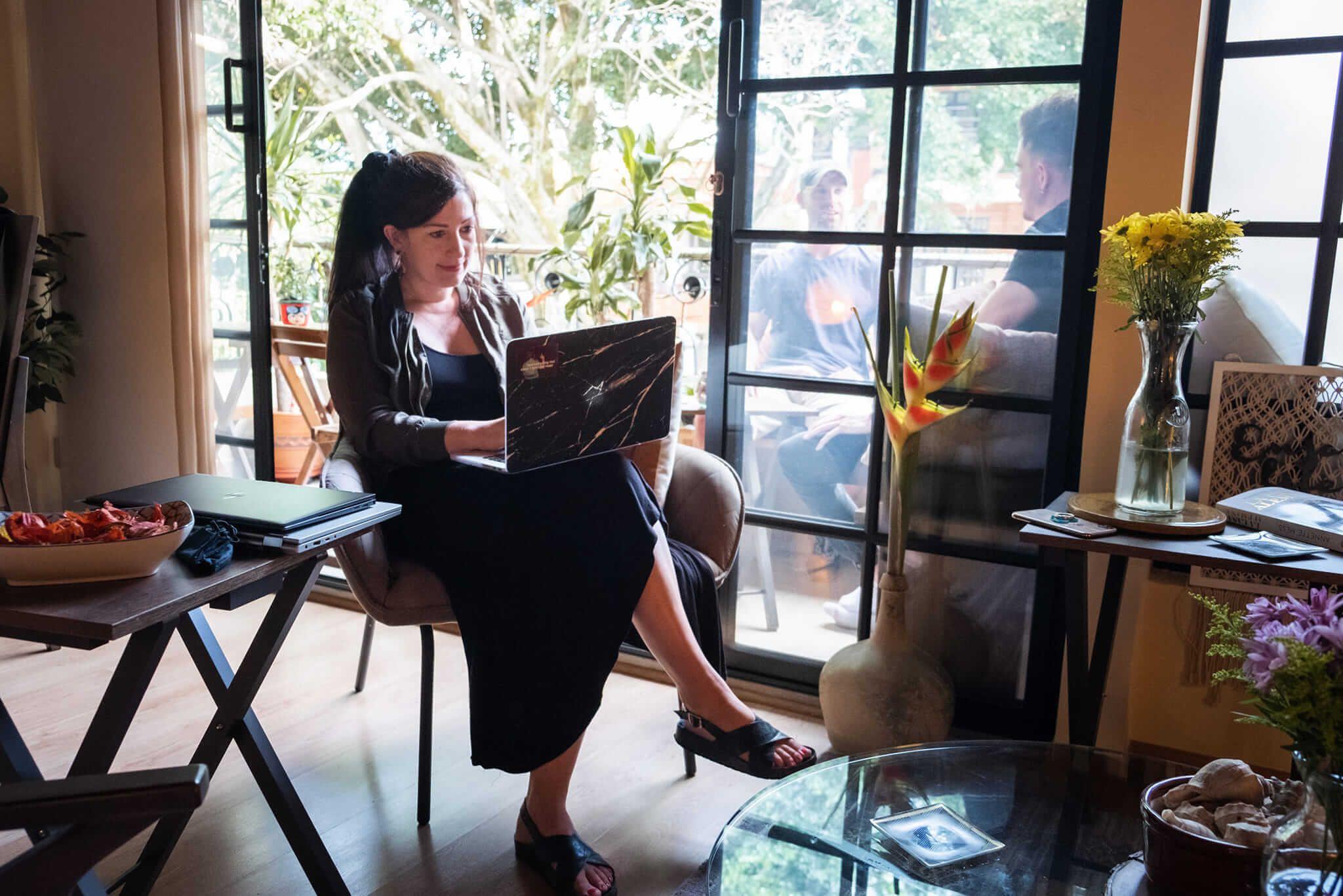 A guest working on a laptop in the coworking/living area with large windows and natural light