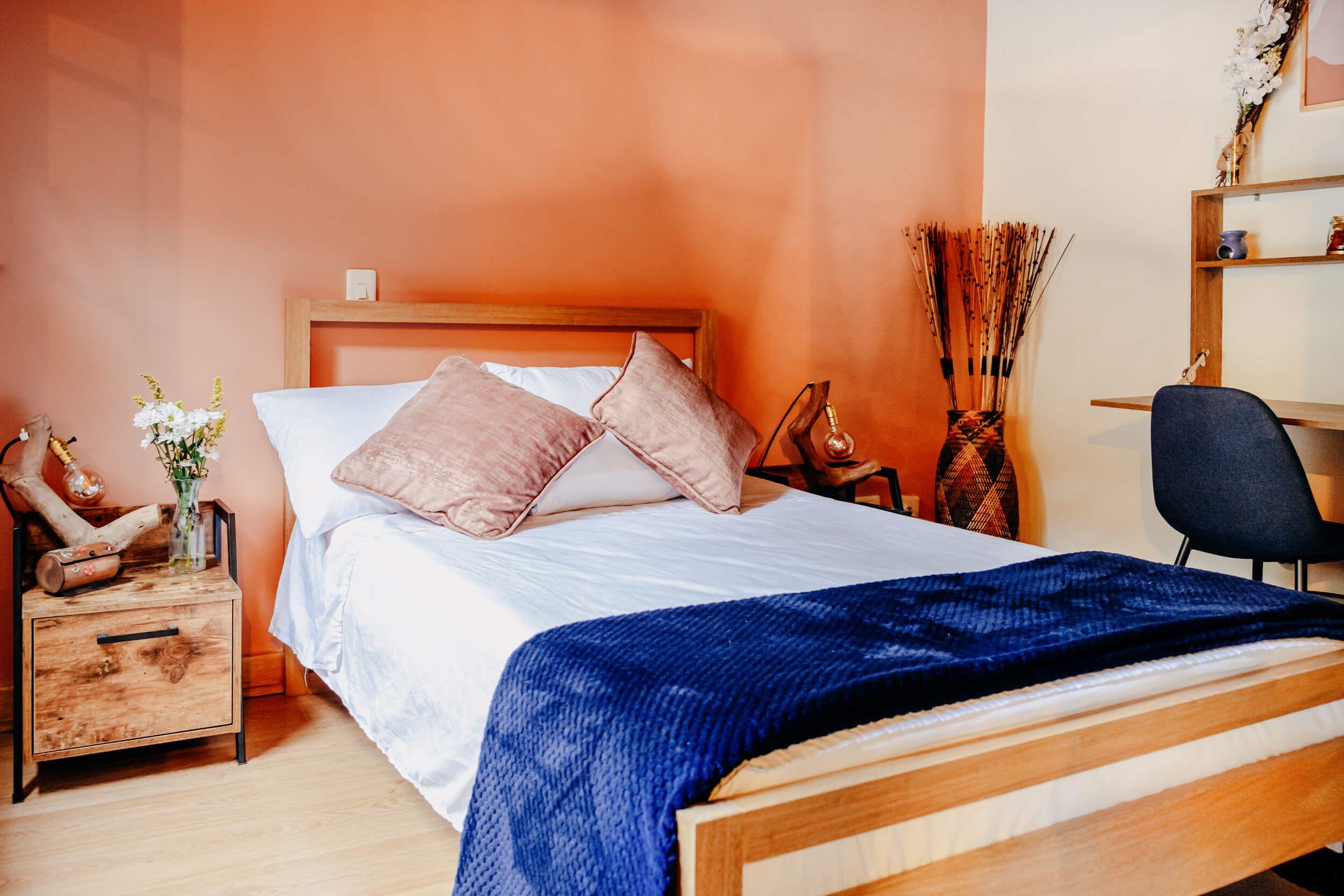 Main view of Bedroom 5 with a queen bed, warm colours, hanging plants, and large modern windows