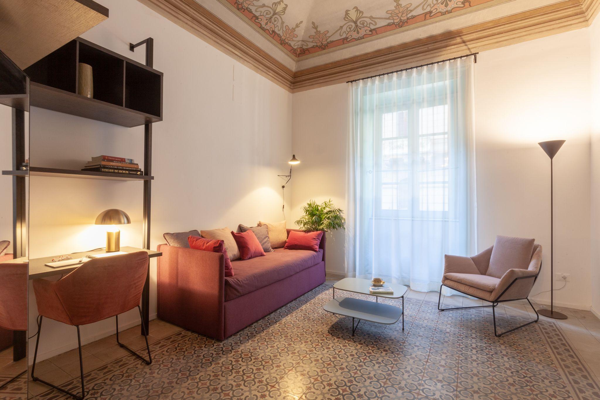 Suite Room living area with maroon sofa, armchair, and frescoed ceiling