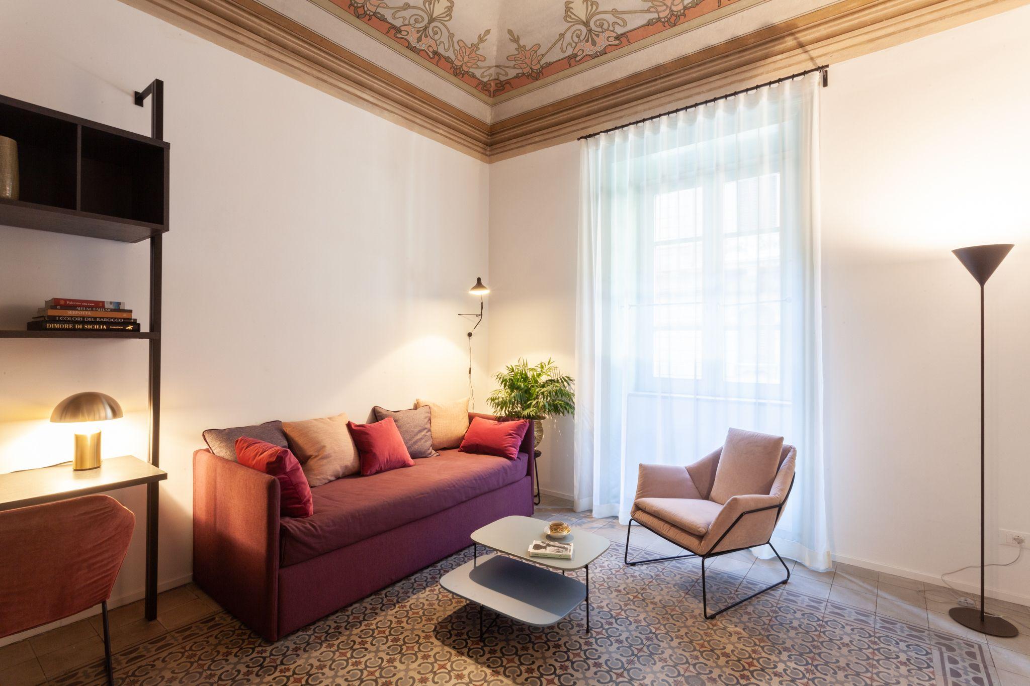 Living room with maroon sofa, armchair, and decorative frescoed ceiling