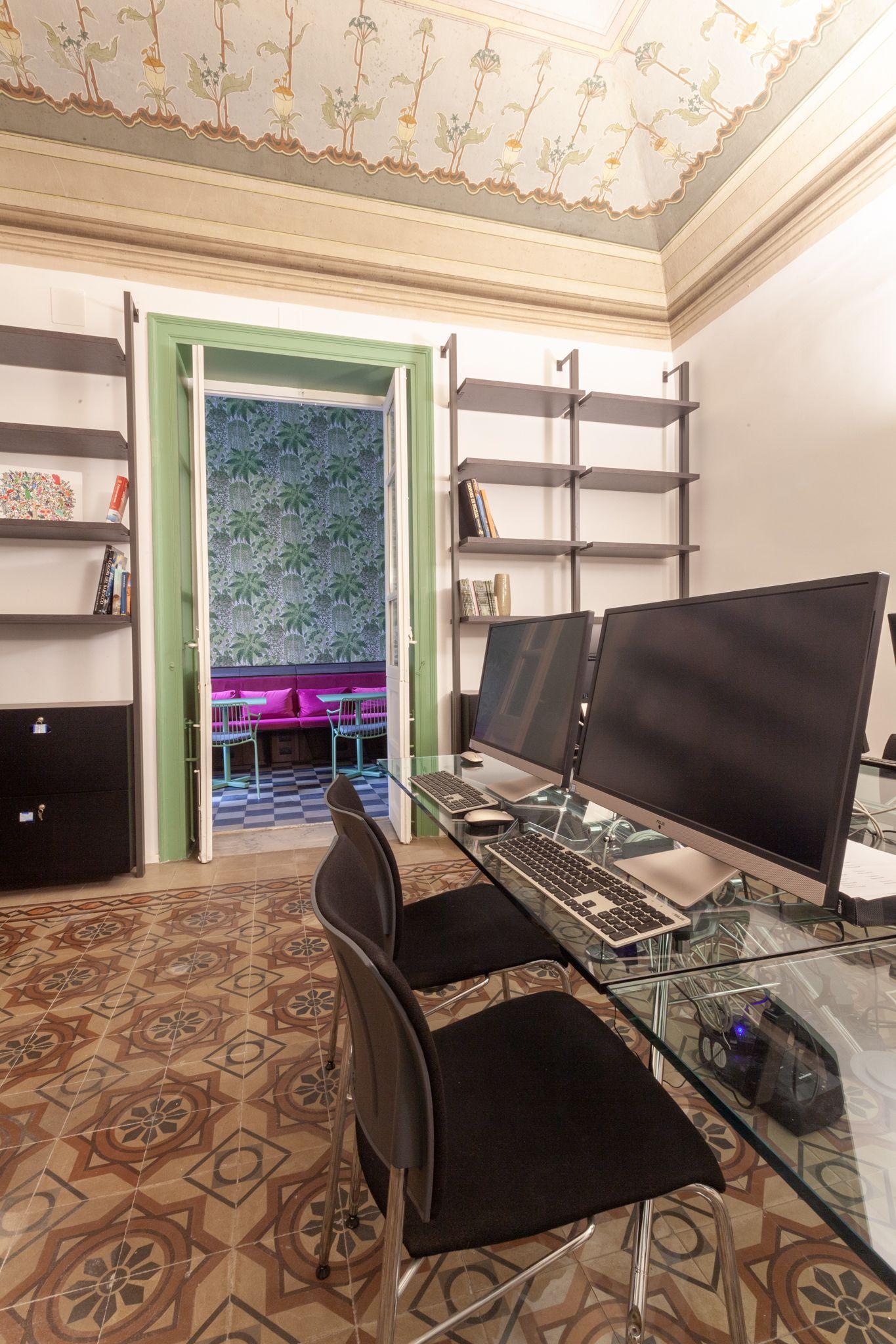 Coworking office with dual monitors, glass desk, and frescoed ceiling, view to relaxation area