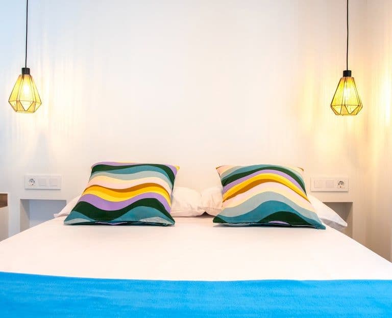 A bed with a blue blanket and lamps in a cozy coliving room