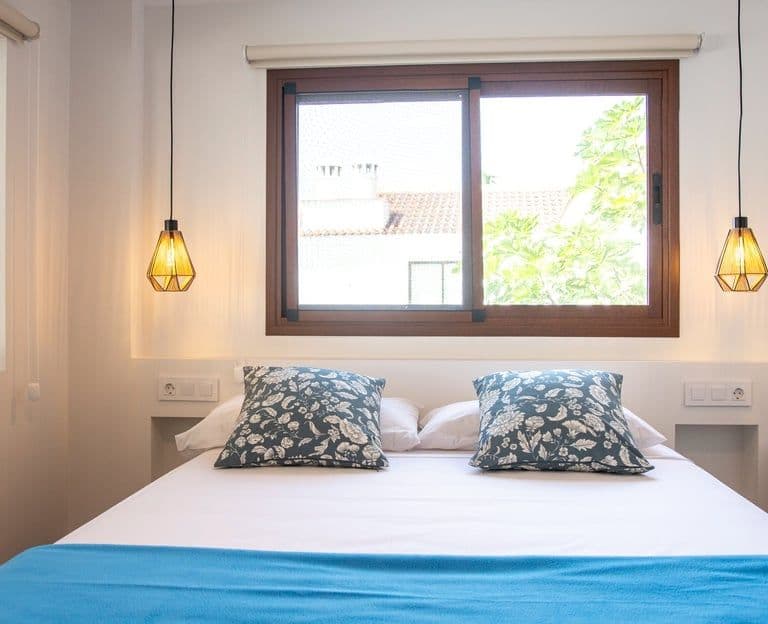 A bed with a blue blanket and a window with privacy for travellers in Tenerife