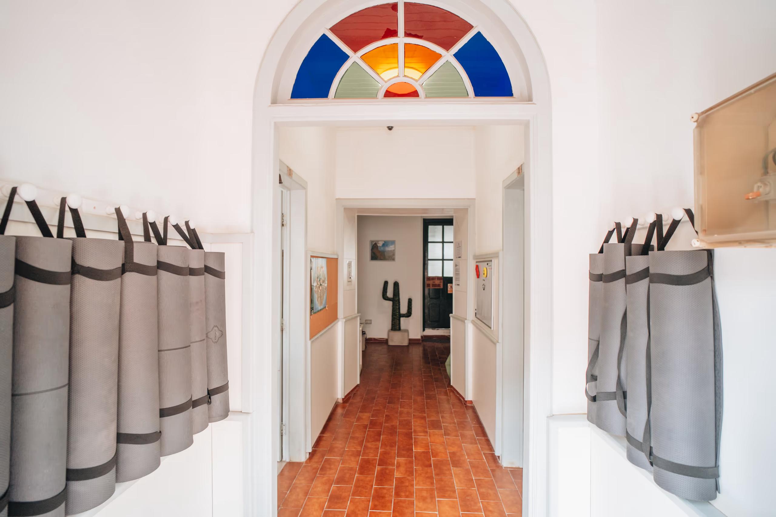 Interior hallway with yoga mats stored on the walls and a colorful stained glass arch at Cactus La Gomera