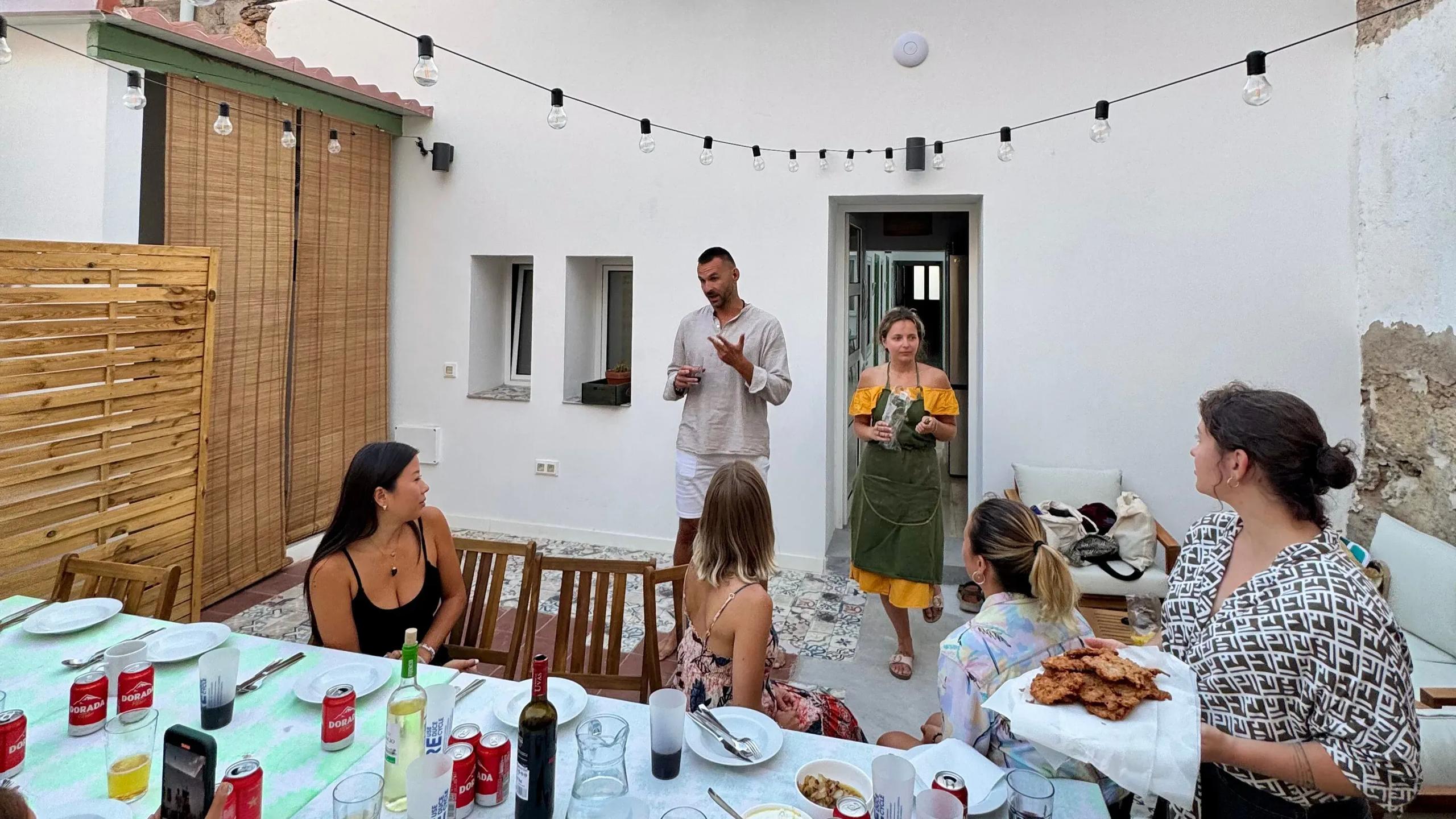 Group of colivers gathered around a table for a BBQ dinner on the outdoor patio, with string lights and BBQ grill visible