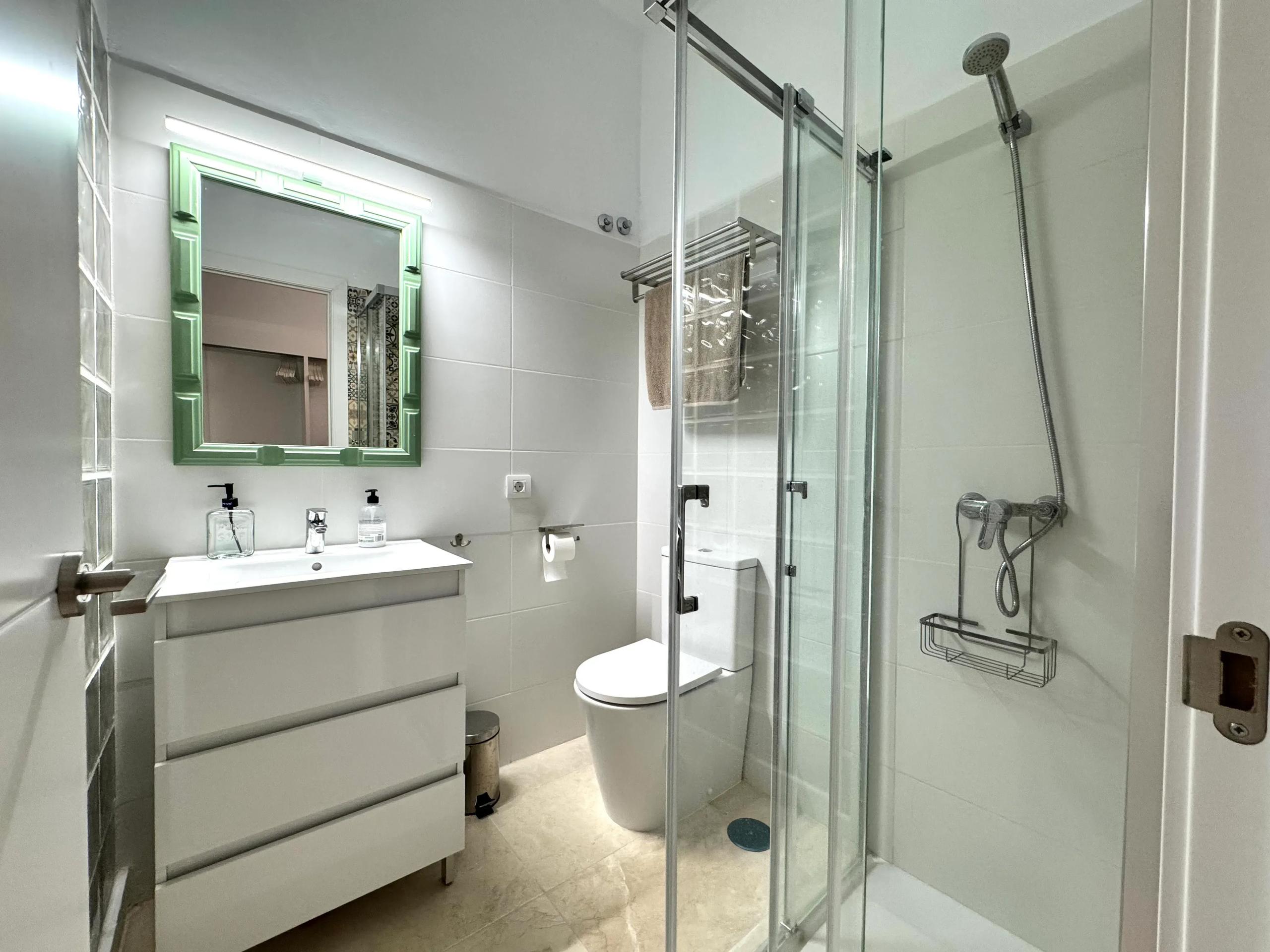 Clean white private bathroom with green-framed mirror, glass shower enclosure and sink