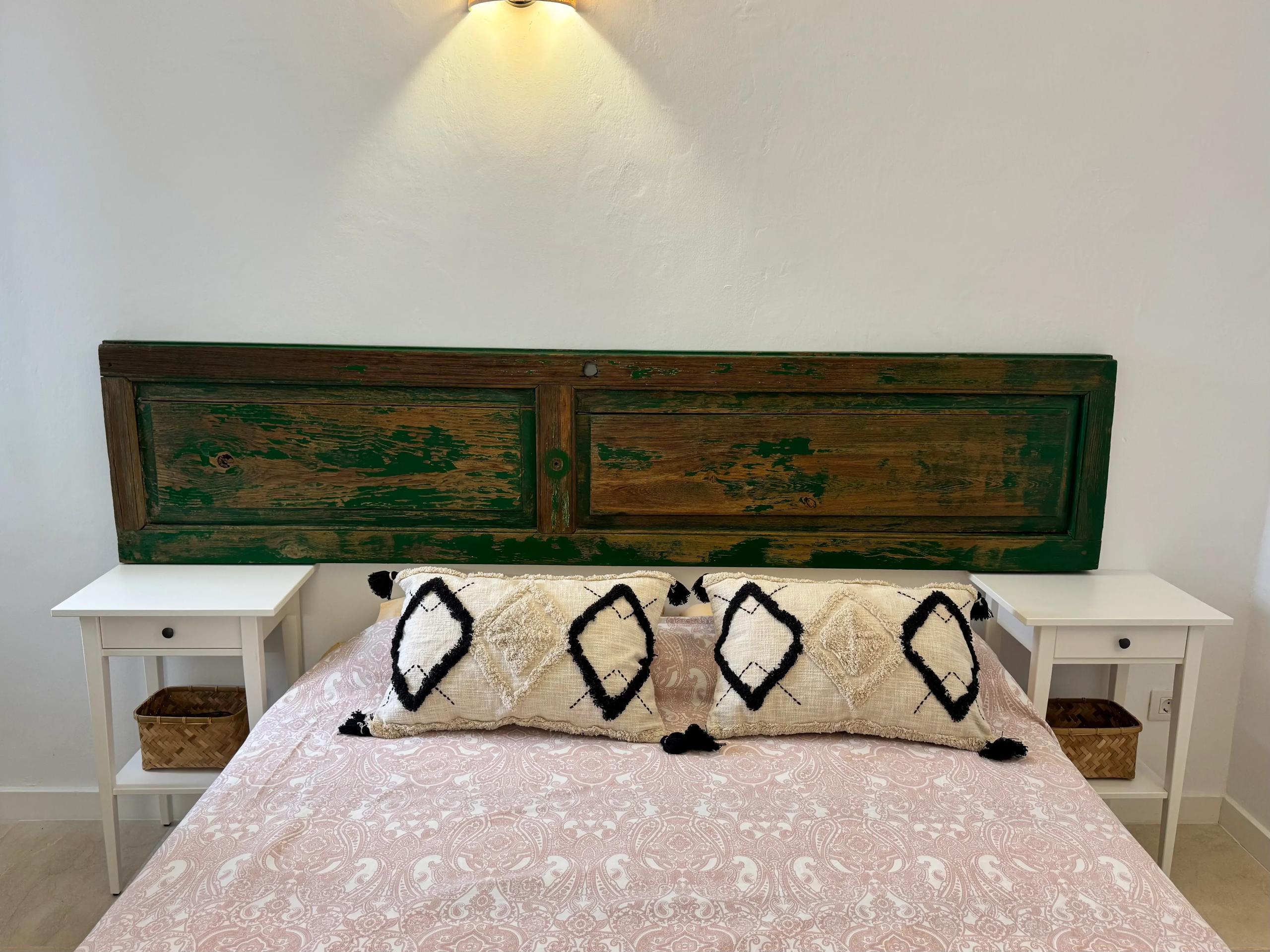 Double bedroom with a large green-painted rustic wooden headboard, pink bedding and white bedside tables