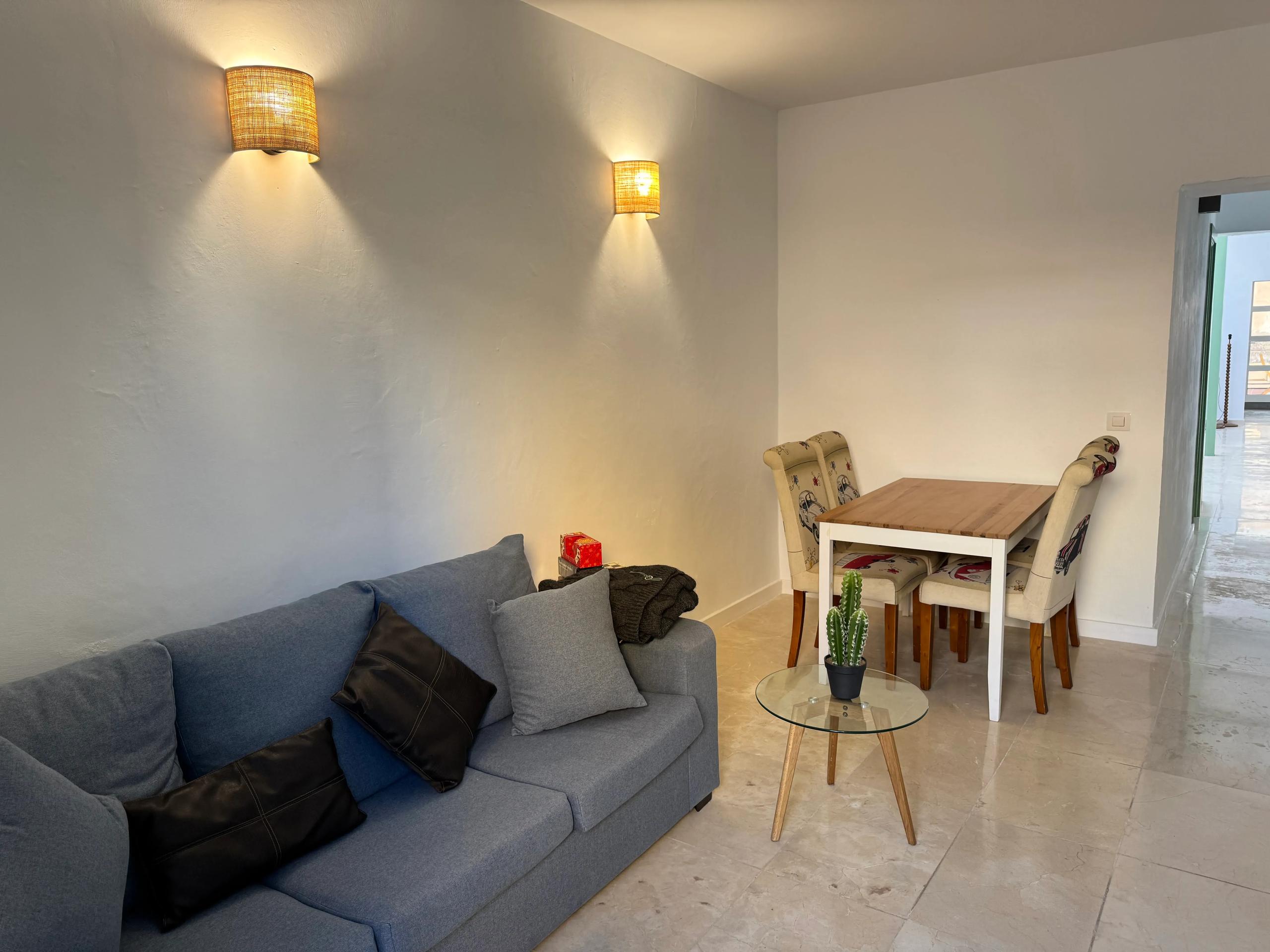 Living room with blue sofa, dining table and chairs, warm wall lighting