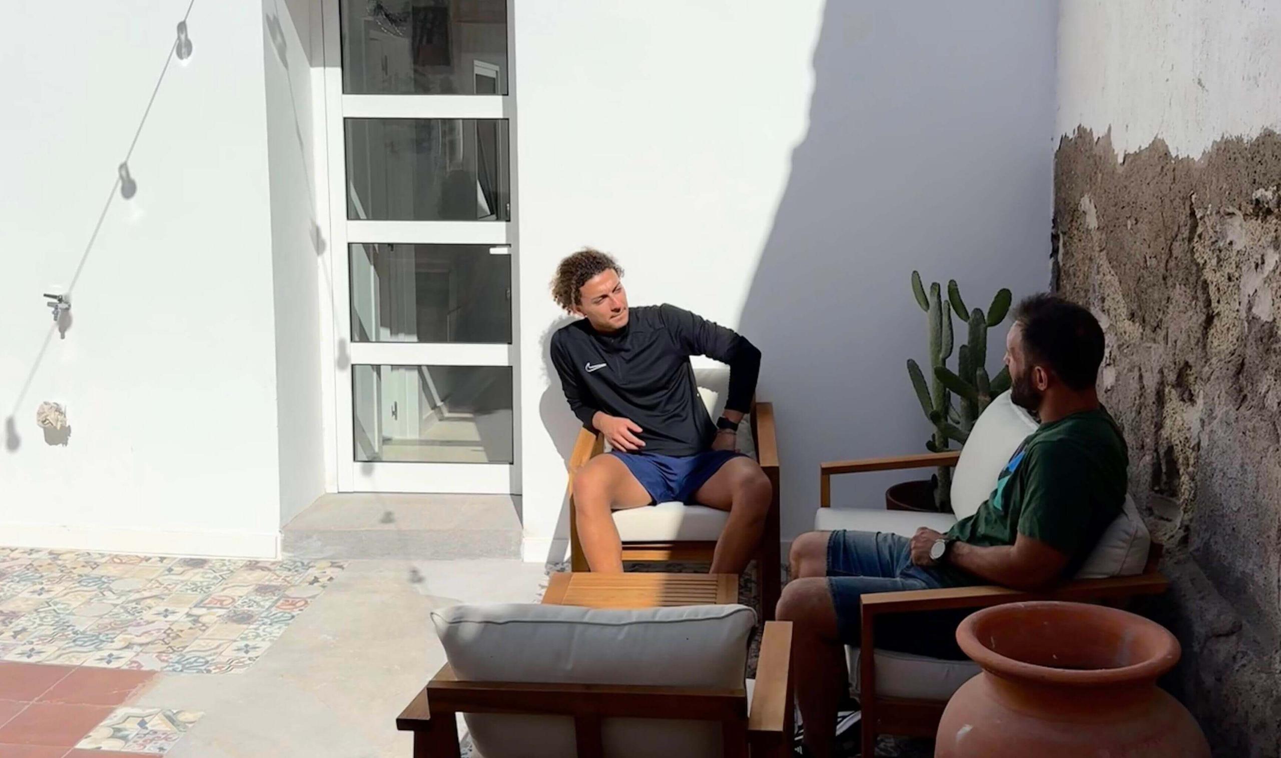 Two colivers chatting on the outdoor patio with wooden armchairs, cactus plants and string lights