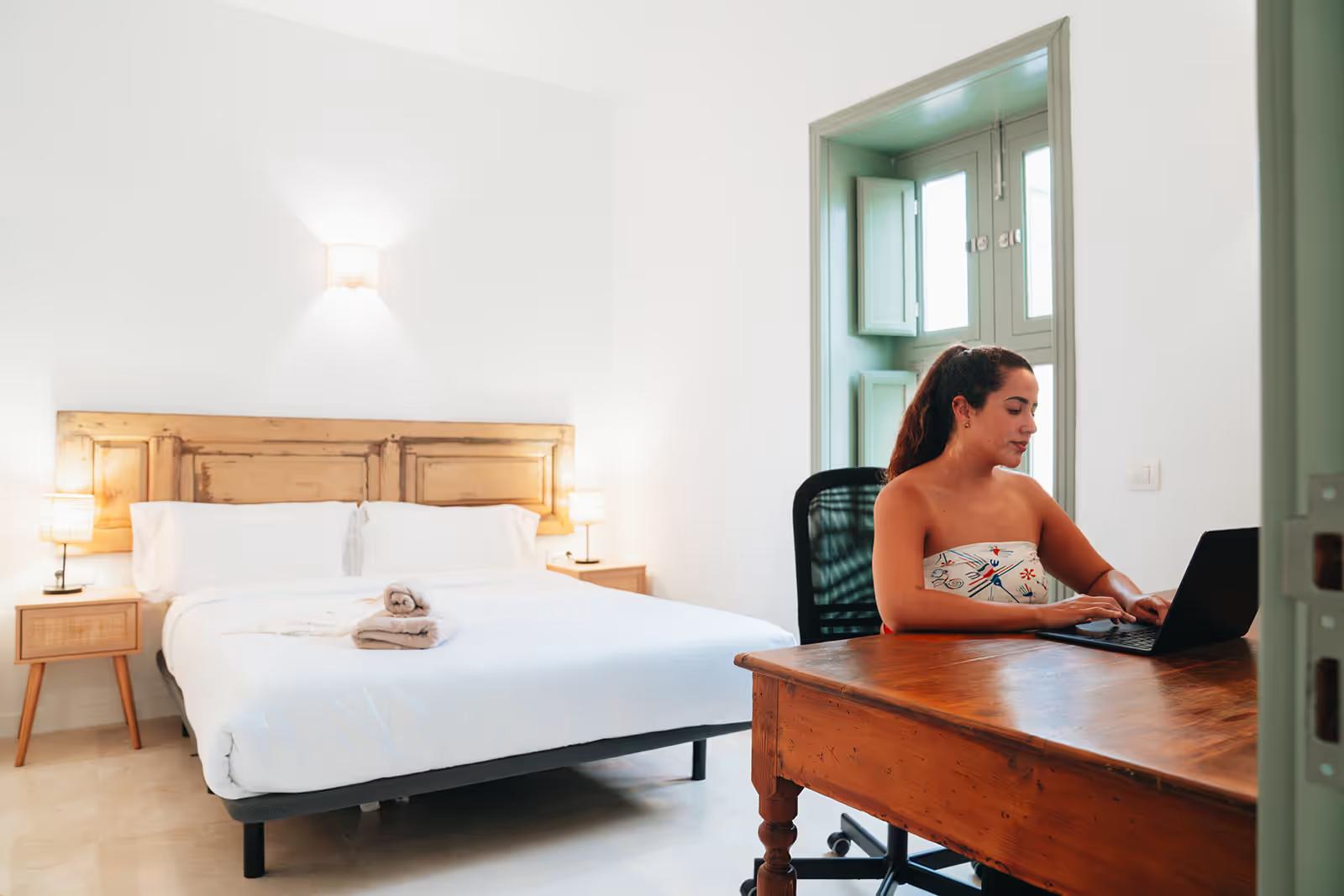 Spacious double bedroom with wooden bed, white bedding, ergonomic desk chair and traditional green-framed window