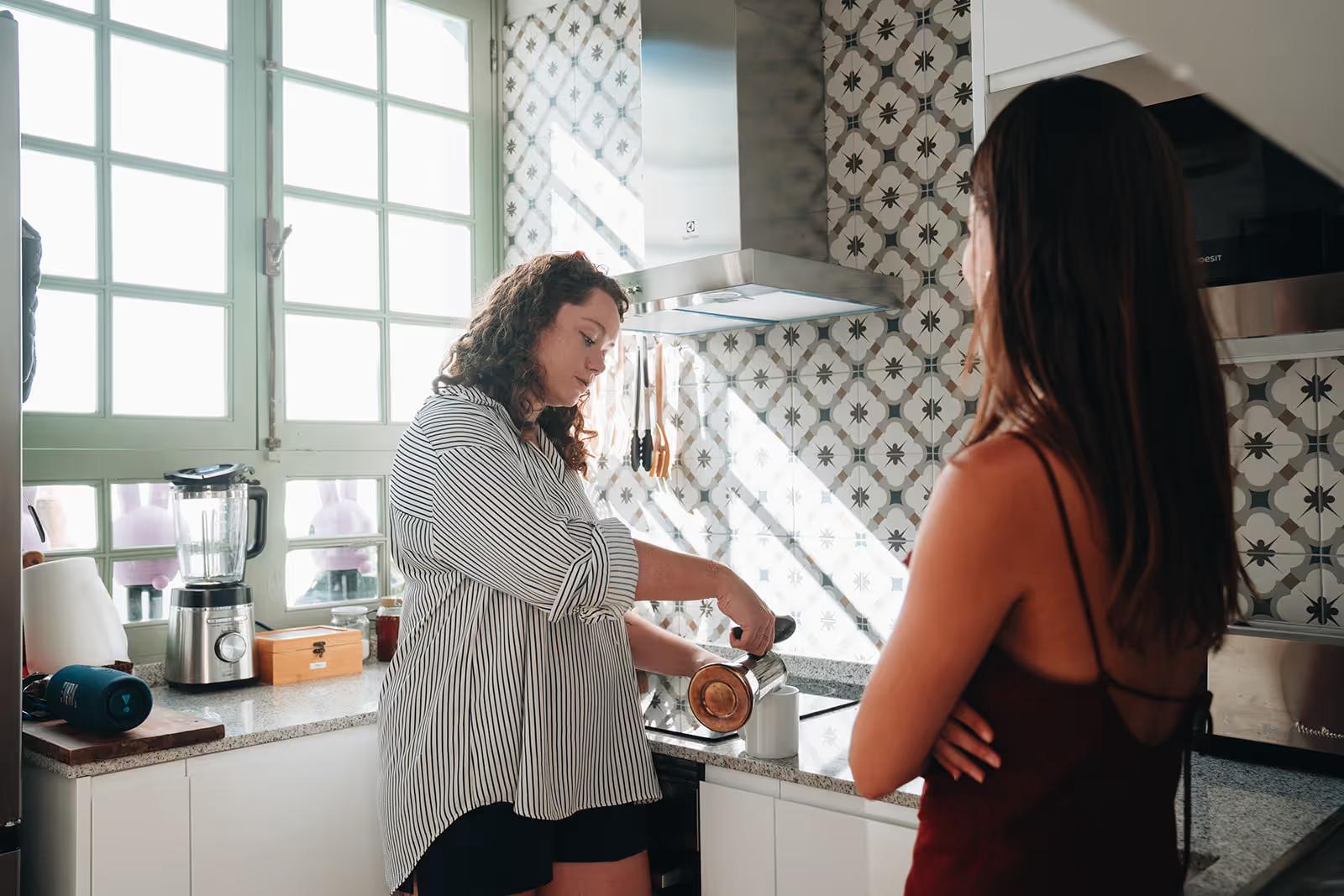 Two women preparing coffee together in the shared kitchen with patterned tile backsplash