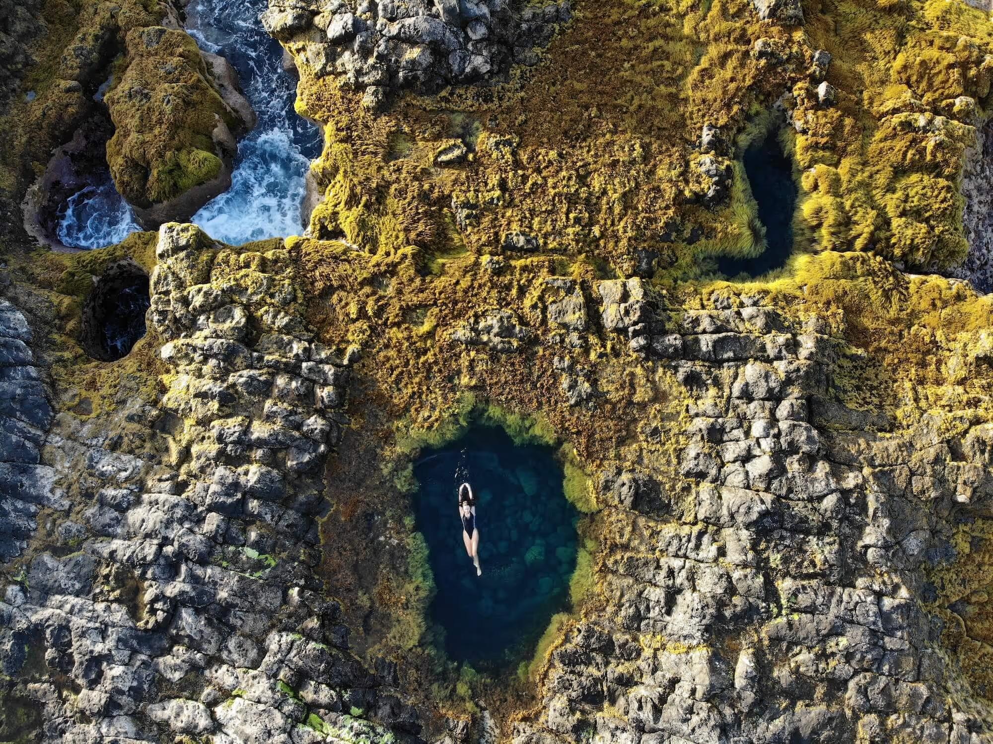 A gorgeous volcanic natural swimming pool by the sea in Tenerife with someone from Cactus Coliving swimming in it