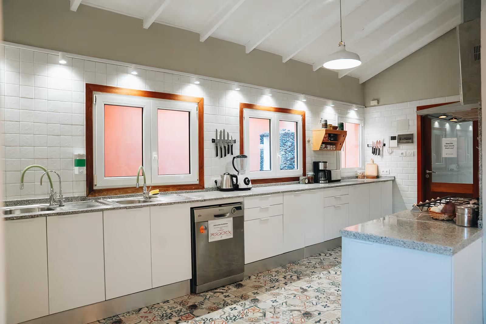 Fully equipped shared indoor kitchen with white cabinets, granite countertops, dishwasher, and patterned tile floor