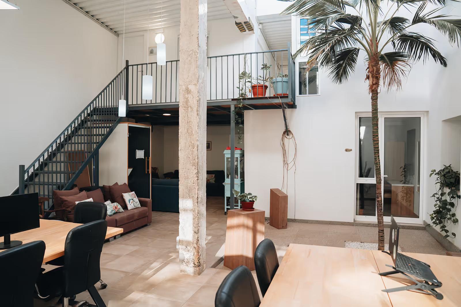 Open interior patio with coworking desks, a palm tree, staircase, and sofa area — the main indoor courtyard