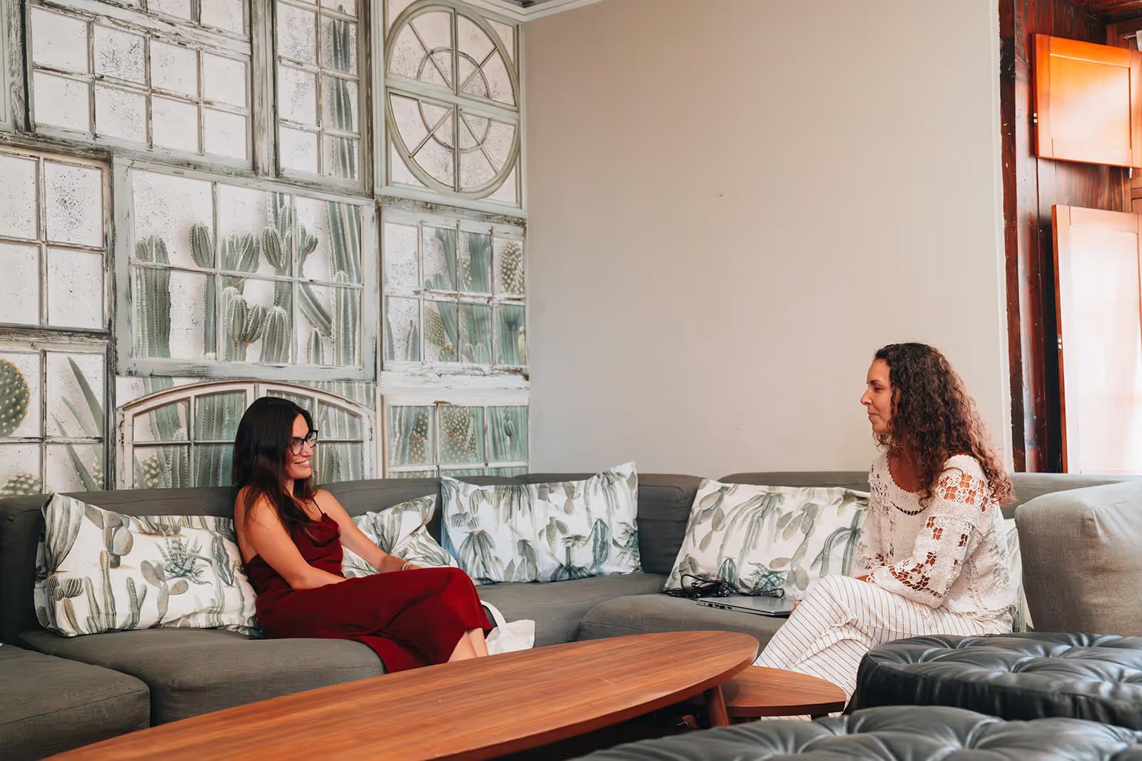 Two women sitting on a grey sofa in the living room with cactus-themed wallpaper mural