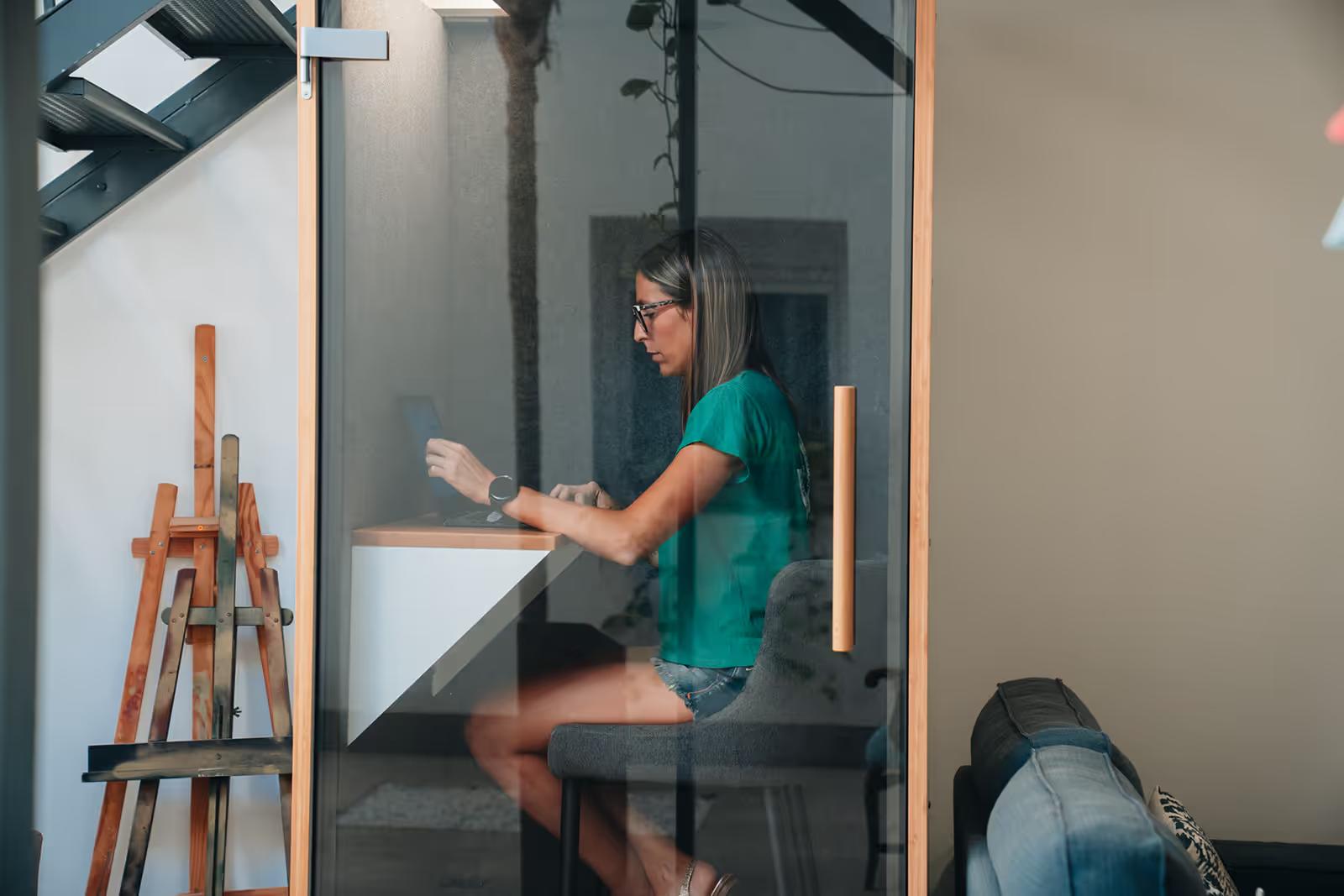 Person working in a glass-walled private conference room with a laptop