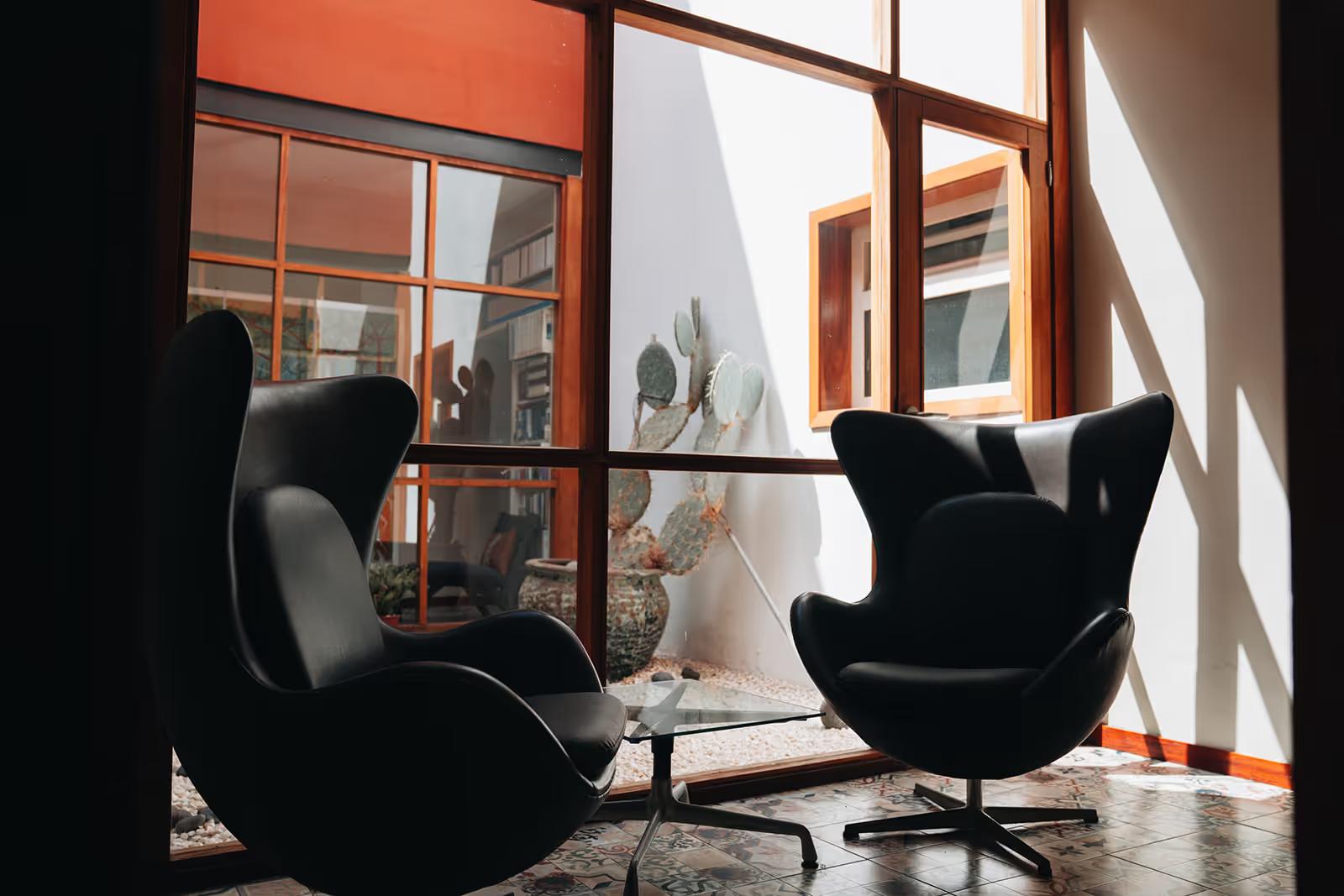 Two black egg chairs in a bright room overlooking the interior patio with a cactus
