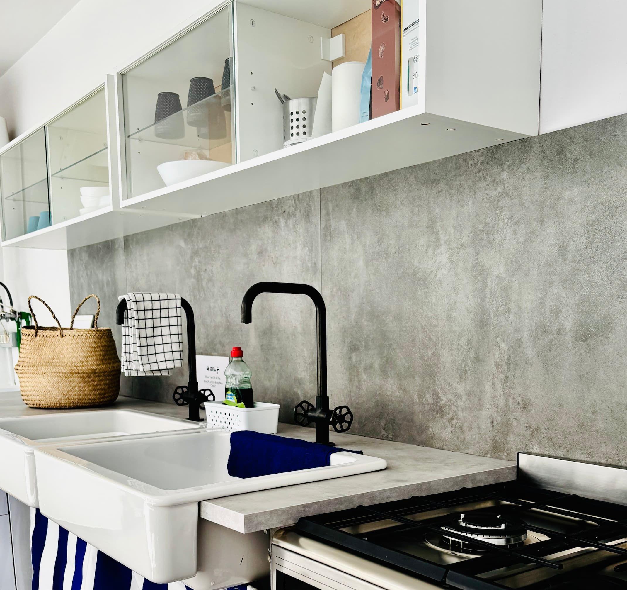 Well-equipped indoor shared kitchen with white cabinets, concrete backsplash, black faucet, and gas stove