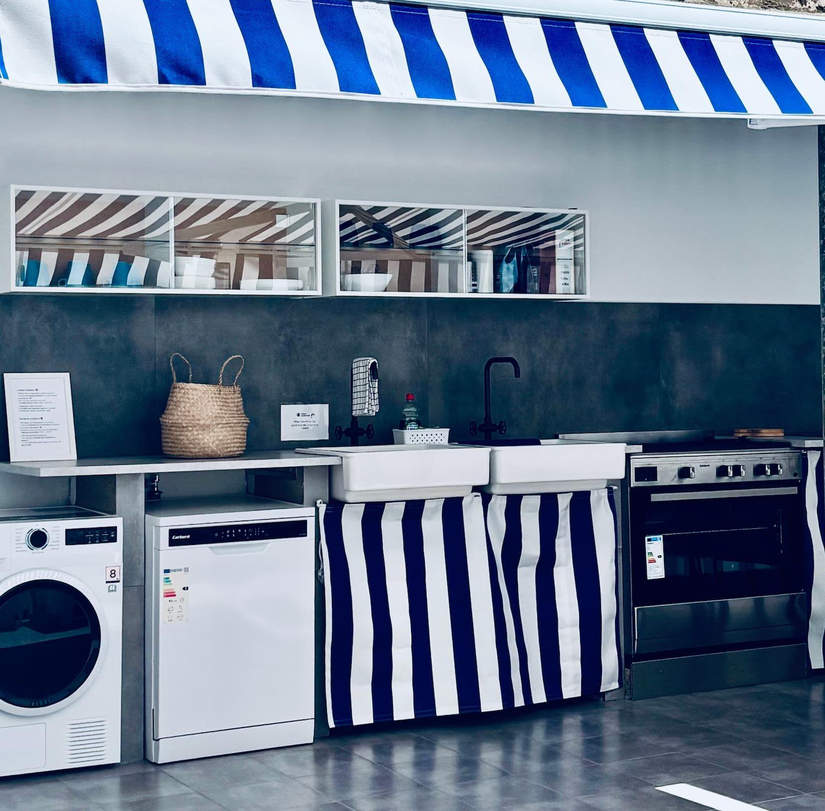 Covered outdoor kitchen with blue and white striped retractable awning, washing machine, dryer, sink, and gas stove